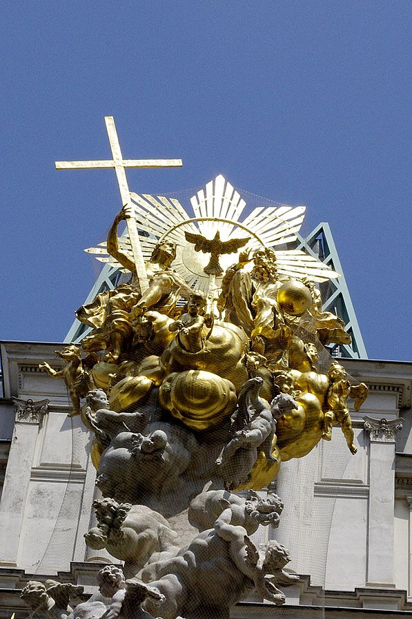 Zdjęcie przedstawia złoty wierzchołek kolumny morowej, na którym umieszczone są postacie Boga Ojca i Jezusa Chrystusa oraz gołębia symbolizującego Ducha Świętego.