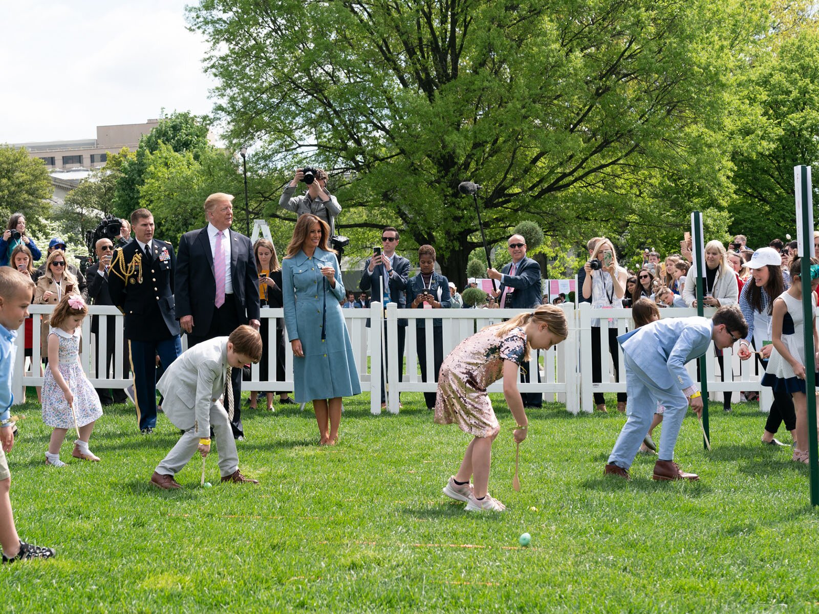 Zdjęcie przedstawia byłego prezydenta Stanów Zjednoczonych z żoną przyjmujących dzieci w swoim ogrodzie. Widoczne są dzieci toczące jajka po trawie. 