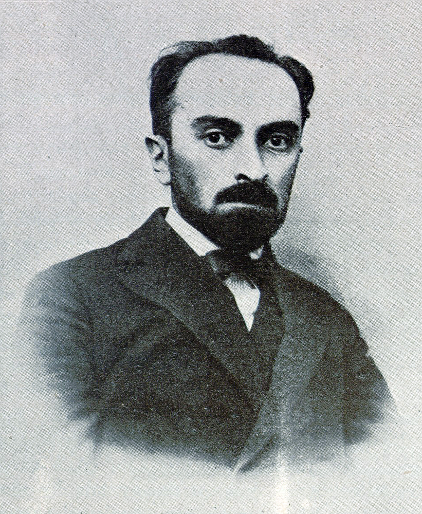 Na czarno‑białej fotografii znajduje się Adam Skwarczyński. Jest on ubrany w ciemny garnitur i muszkę. Ma krótkie ciemne włosy, brodę i duże oczy. 