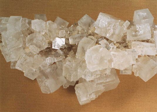 Kolorowa fotografia przedstawia kryształy soli w dużej bryle. Mają one kształty geometryczne, są przezroczyste. 