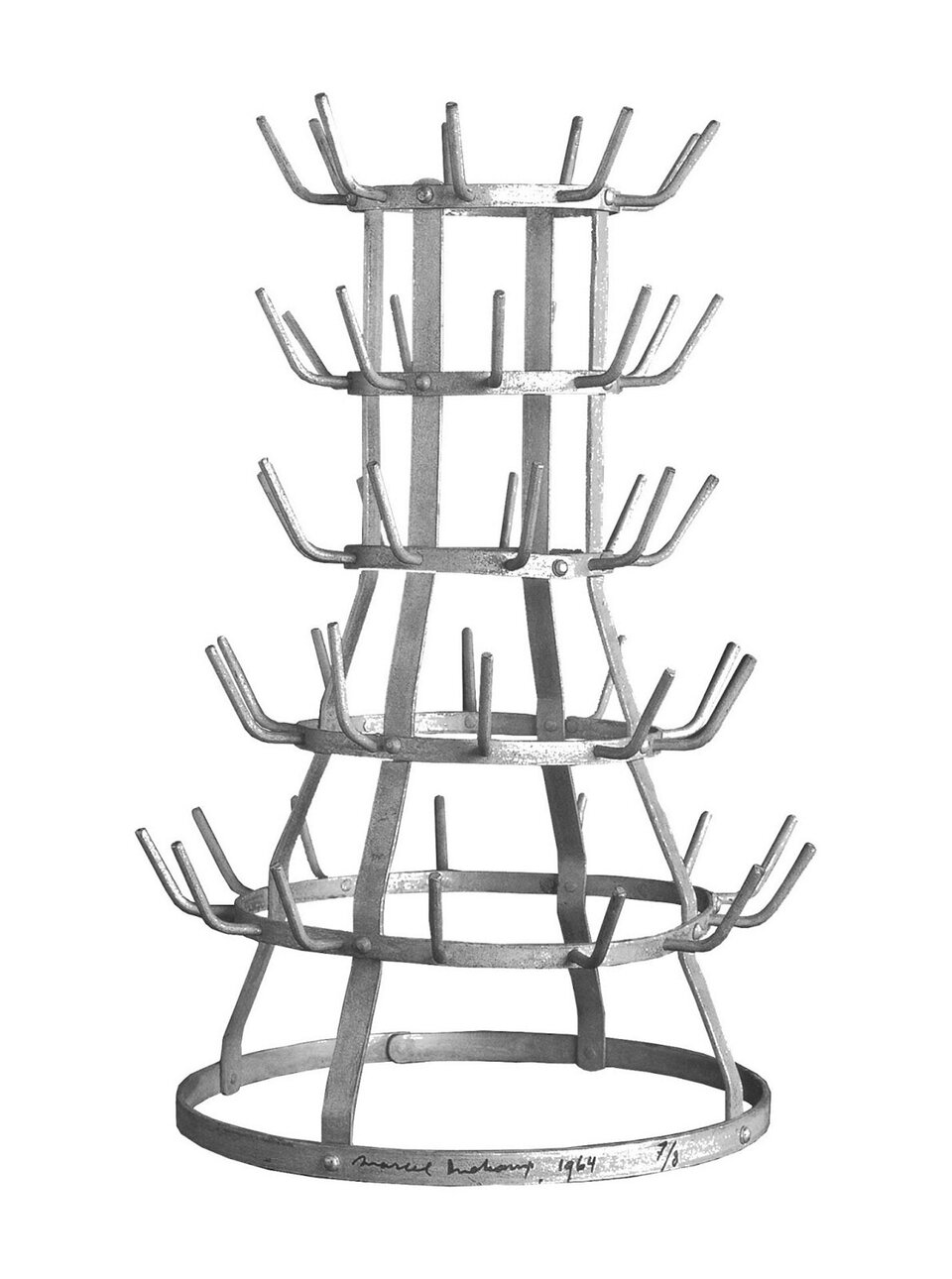 Ilustracja przedstawia konstrukcję „Suszarkę do butelek”, autorstwa Marcela Duchampa. Jest to metalowa konstrukcja składająca się z sześciu okręgów o różnej wielkości połączonych ze sobą. Okręgi układają się poziomo. Na spodzie jest największy okrąg, a kolejne są coraz mniejsze. Koła połączone są czterema wygiętymi, metalowymi listwami stojącymi w pionie. Z okręgów, za wyjątkiem pierwszego wystają metalowe pręty, które przypominają wieszaczki. Są umiejscowione w odstępach dookoła okręgu.