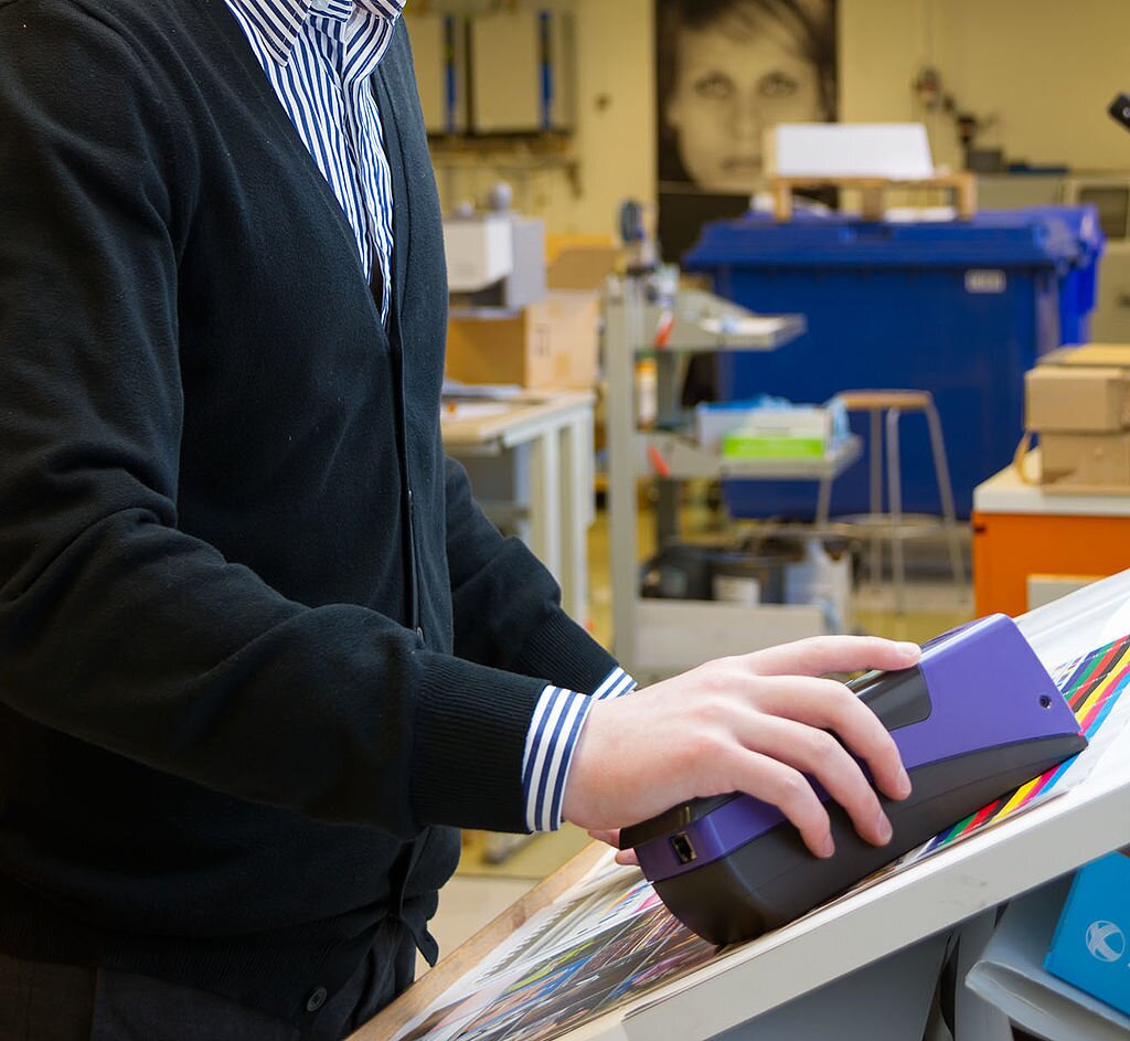 Zdjęcie przedstawia osobę trzymającą w ręce spektrofotometr podczas sprawdzania wydruku w celu kalibrowania drukarki.