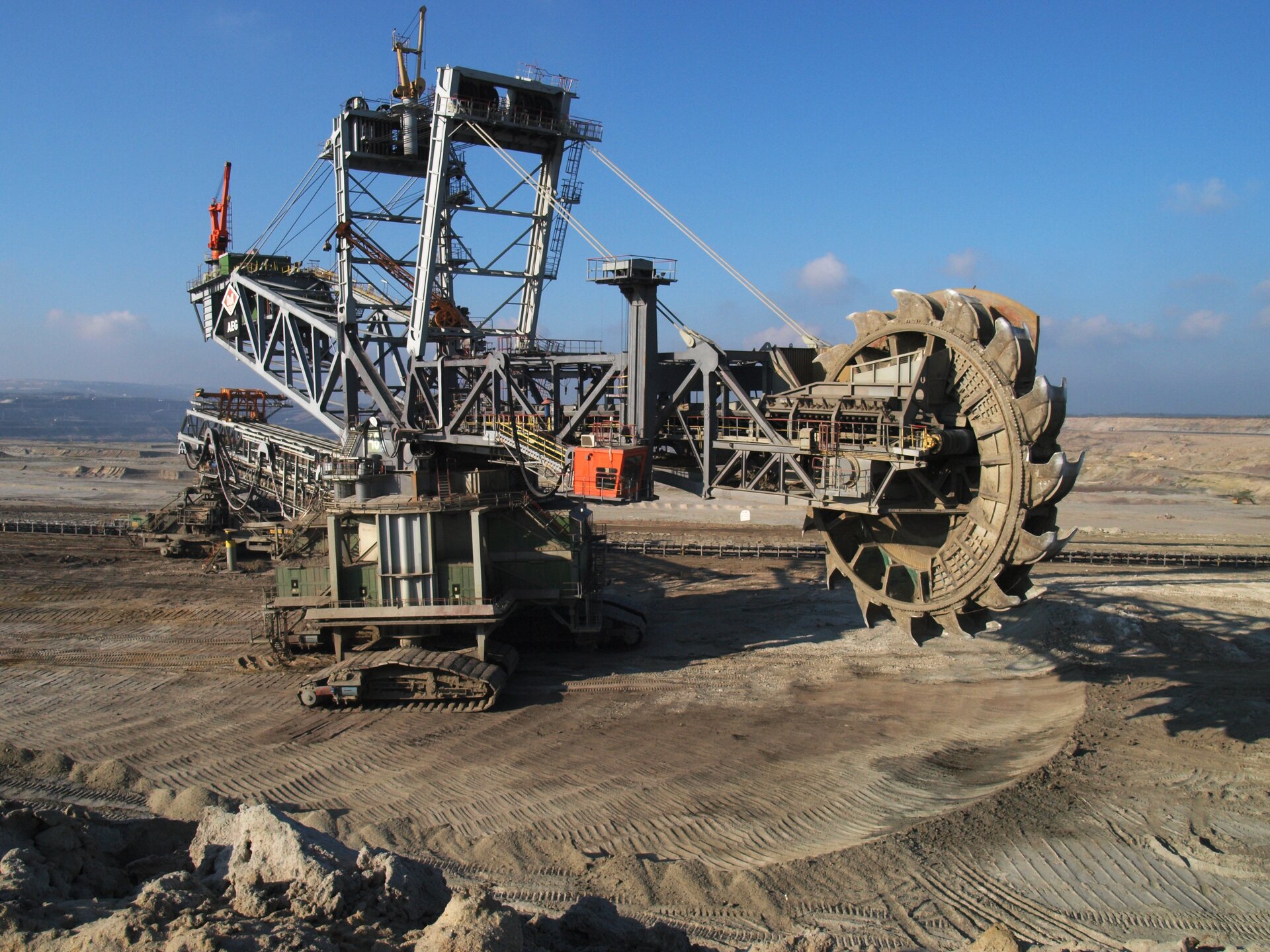 Zdjęcie przedstawia wieloczerpakową koparkę podpoziomową. Maszyna składa się z wielu naczyń kopiących – czerpaków, które umiejscowione są na kole (w postaci koła zębatego), na łańcuchach i stelażach.

Opisy obiektów prezentowanych na grafikach są załączone w treści galerii zdjęć.