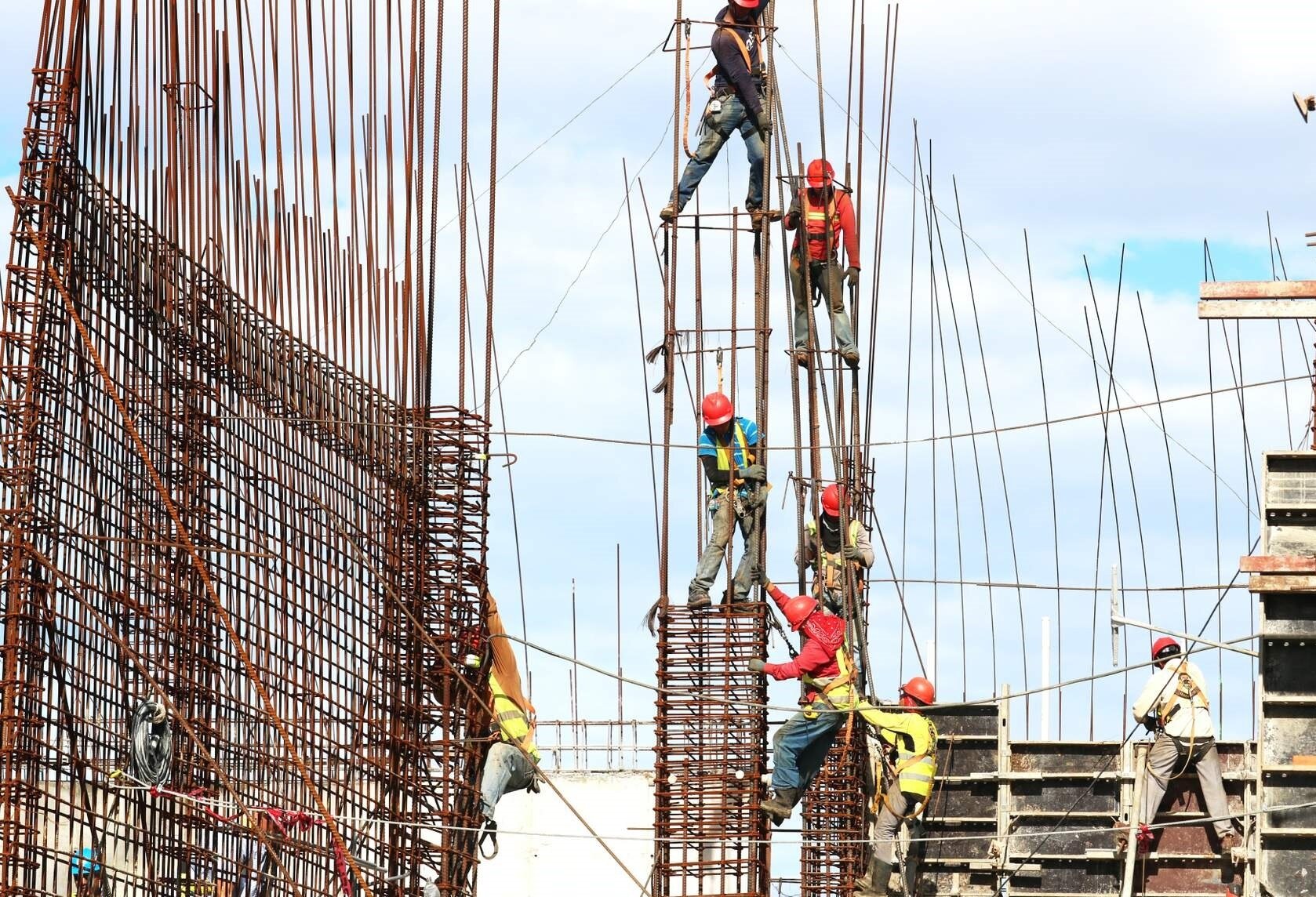 Zdjęcie pierwsze, podpisane pasowanie elementów. Fotografia przedstawia budowę wysokich metalowych zbrojeń. Na zdjęciu jest widocznych ośmiu pracowników.