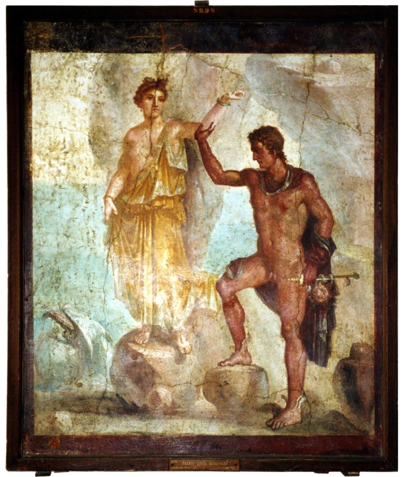 Ilustracja przedstawia fresk pompejański zatytułowany: „Perseusz i Andromeda”. W centrum obrazu ukazana jest młoda kobieta stojąca na kamieniu. Jest ubrana w żółtą szatę. Lewe ramię uniesione do góry podtrzymuje stojący obok niej nagi mężczyzna. Z tyłu ma przerzucony płaszcz; w lewej ręce trzyma głowę Meduzy.