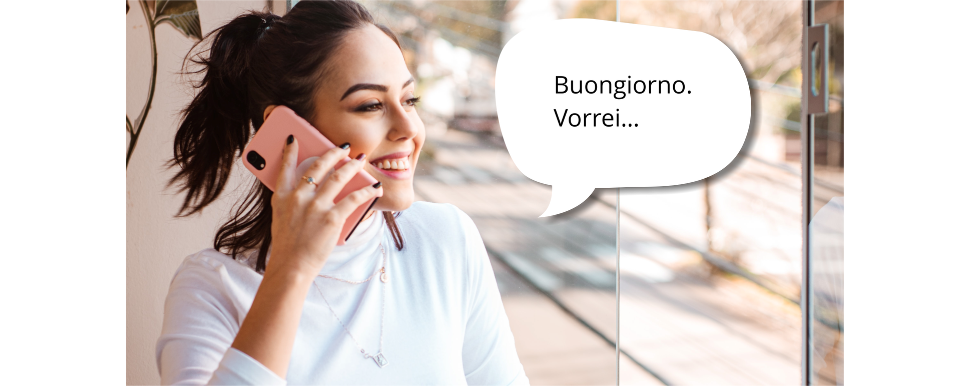 Zdjęcie przedstawia uśmiechniętą dziewczynę, która trzyma w dłoni telefon przy uchu. Dziewczyna ma ciemne włosy spięte z tyłu. Dziewczyna znajduje się w pomieszczeniu przy oknie. W tle widoczna jest ulica. Obok niej znajduje się napis w dymku: Buongiorno. Vorrei...