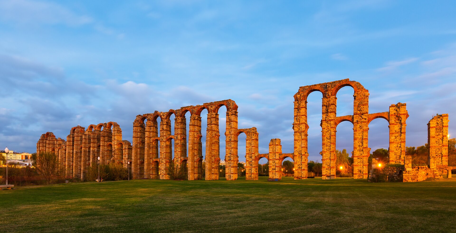 Ilustracja przedstawia rzymski akwedukt w Meridzie w Hiszpanii. Na polanie rozciąga się długi akwedukt, umieszczony na wysokich arkadach. Filary arkad są poprzecinane trzema rzędami łuków. Kamienna budowla jest zniszczona, brakuje części elementów.