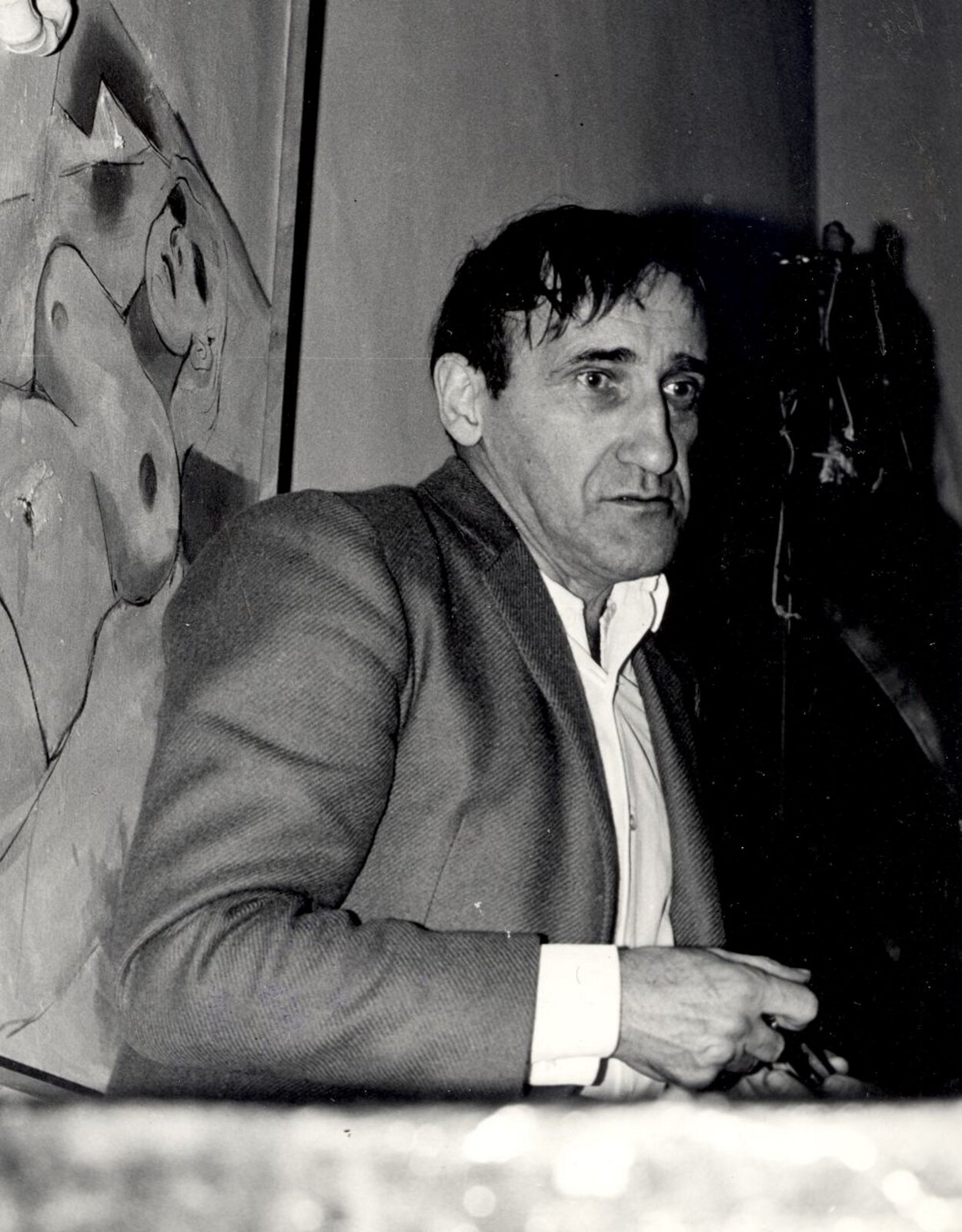 Ilustracja przedstawia czarno-białe zdjęcie Tadeusza Kantora. Mężczyzna ma zdziwiony i zmęczony wyraz twarzy. Ubrany jest w białą koszulę i szarą marynarkę.