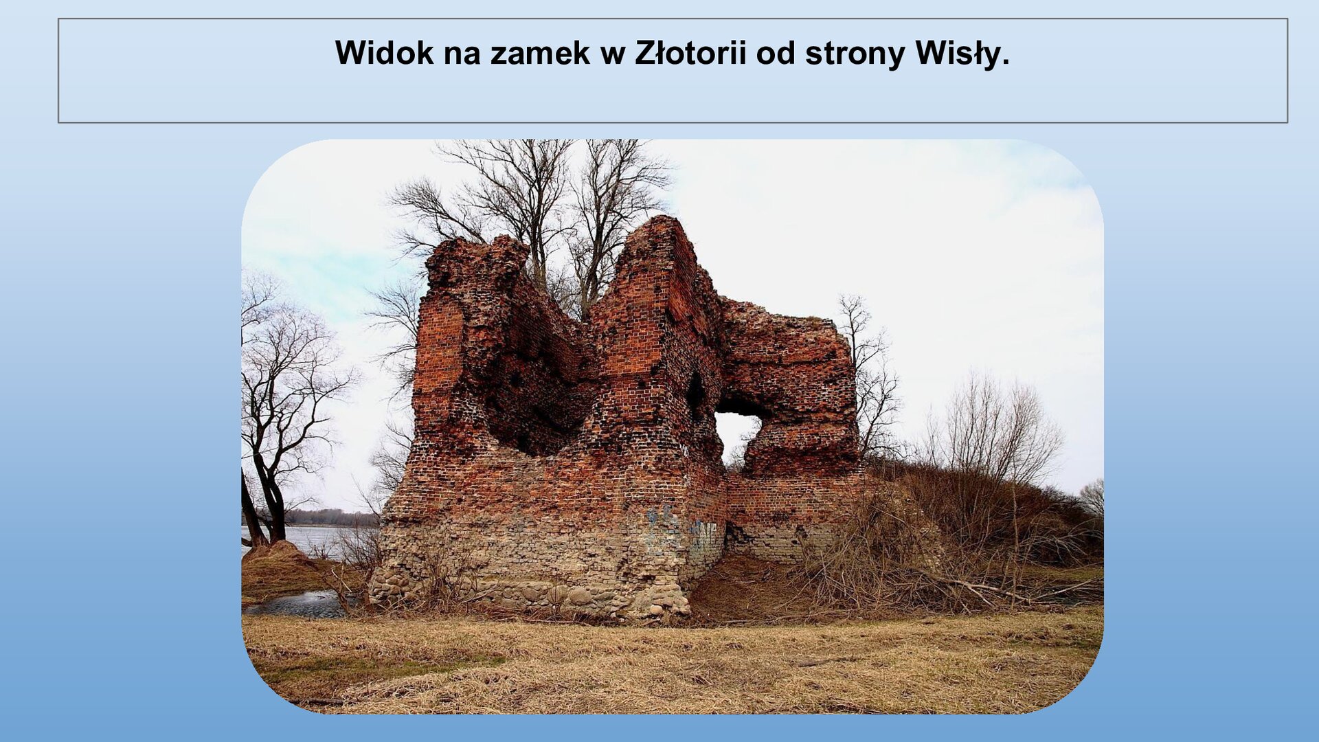 Niebieski slajd. U góry nagłówek: „Widok na zamek w Złotorii od strony Wisły”. Niżej zdjęcie przedstawiające fragment ruin zamku wykonanego z czerwonej cegły. W ścianach zamku otwory. Zamek nie ma dachu. W tle drzewa bez liści.
