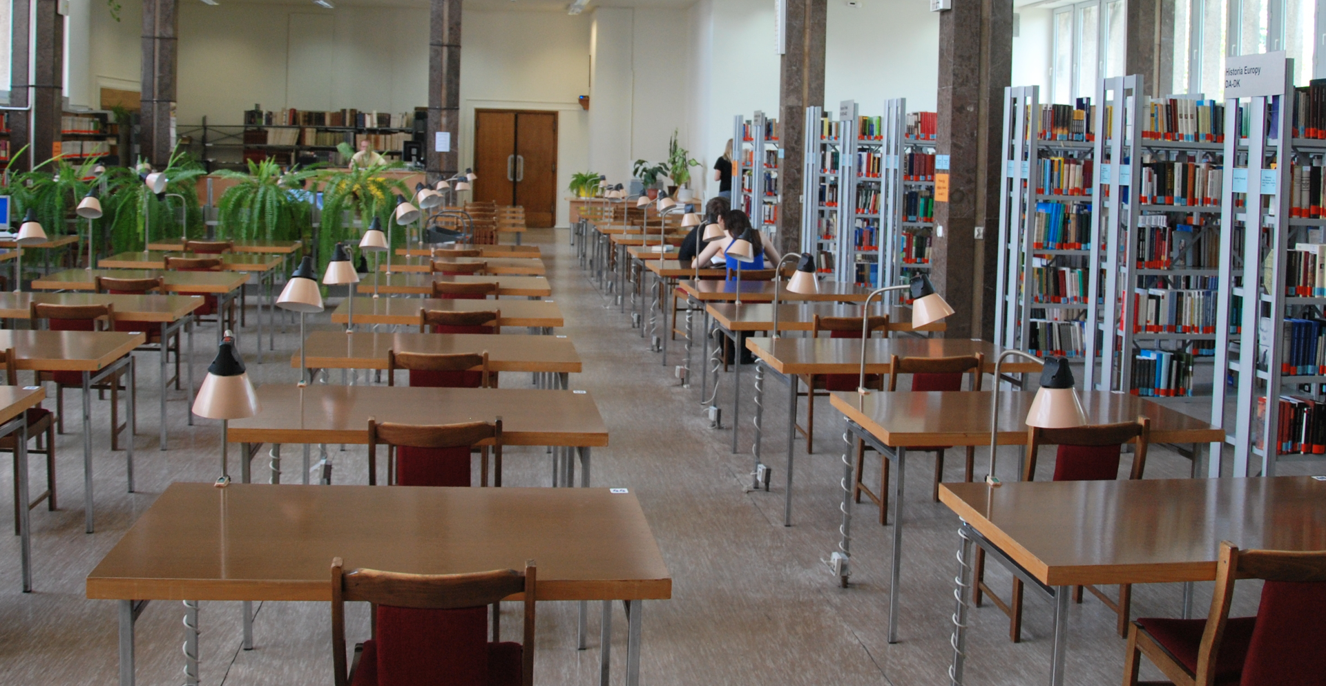 Zdjęcie przedstawia stoły z krzesłami w bibliotece.