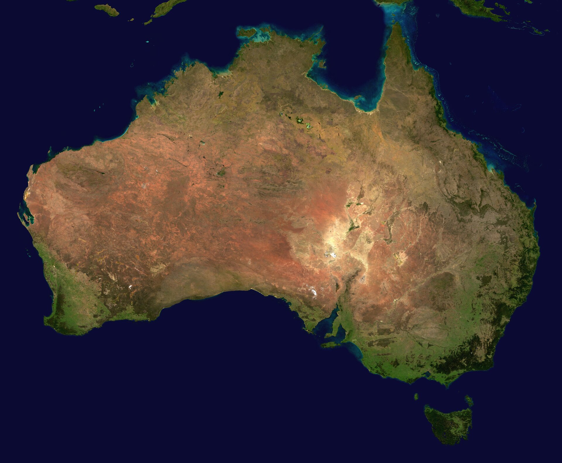 Na zdjęciu satelitarnym kontynent Australii, widoczne tereny zielone nad brzegiem morza i brunatne oraz żółte wewnątrz kontynentu. Rozczłonkowana linia brzegowa na wschodzie kontynentu.