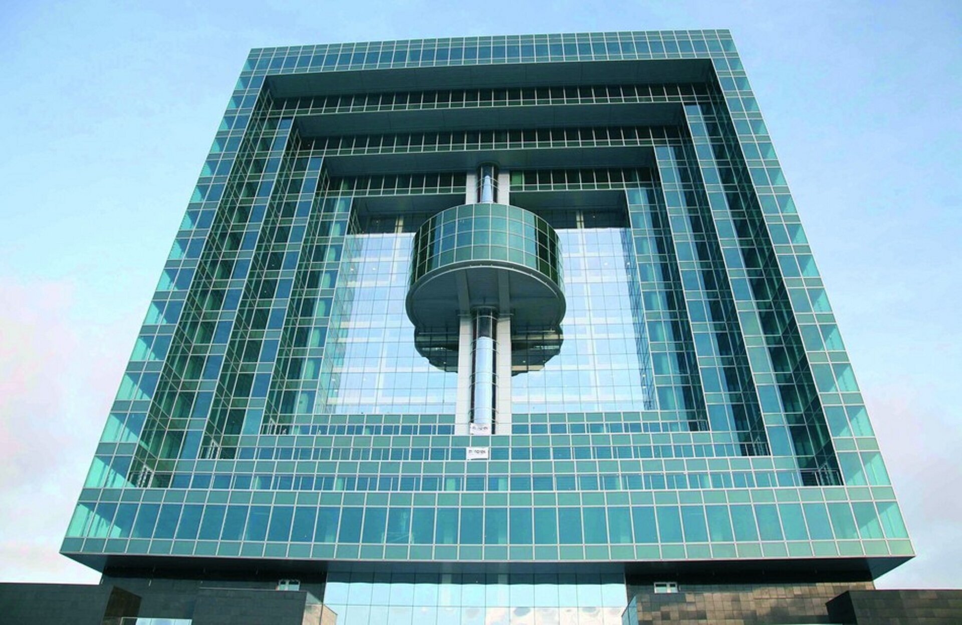 Ilustracja przedstawia Avilon Plaza w Moskwie. Jest to budynek ze szklaną elewacją. Konstrukcja to cztery kwadraty wpisane jeden w drugi. W najmniejszym z nich są trzy filary, a na środku nich półokrągła część wystająca z budynku również pokryta szkłem. Szklana elewacja ma kolor zielonkawo-niebieski. W tle jasne błękitne niebo.