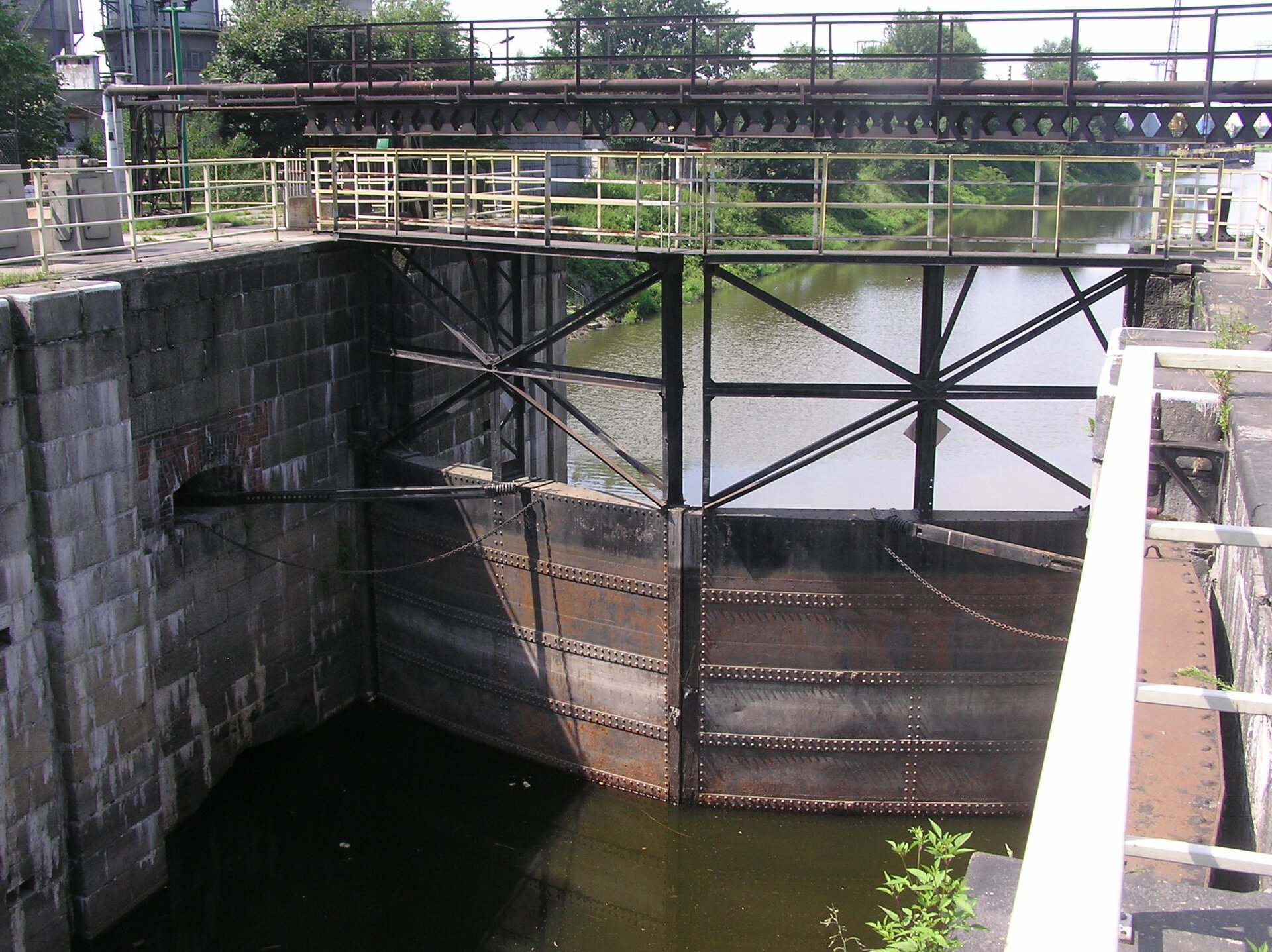 Widok komory w kierunku wrót dolnych. Ściany komory kanału mają wysokość prawie 9 m i wykonane są z bloków granitu. Do zamykania i otwierania bramy przeciwpowodziowej służą wrota wykonane ze stali konstrukcji nitowanej. Poziom wody rzeki jest niski.
