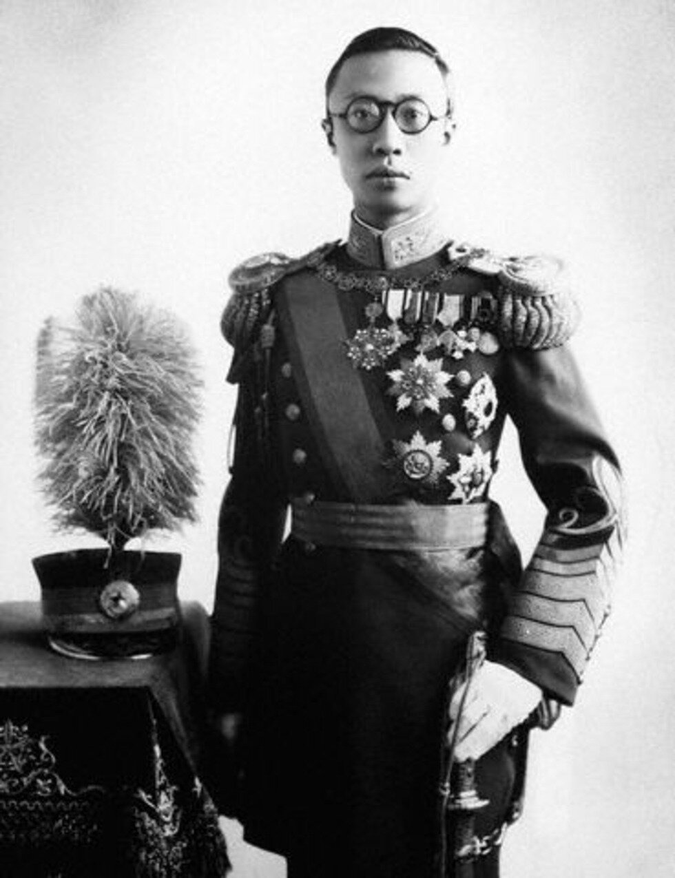 Zdjęcie przedstawia mężczyznę o azjatyckiej urodzie. Ma krótkie włosy oraz okulary w ciemnych oprawkach. Ubrany jest w mundur pełen medali i orderów. Trzyma w ręku szablę.