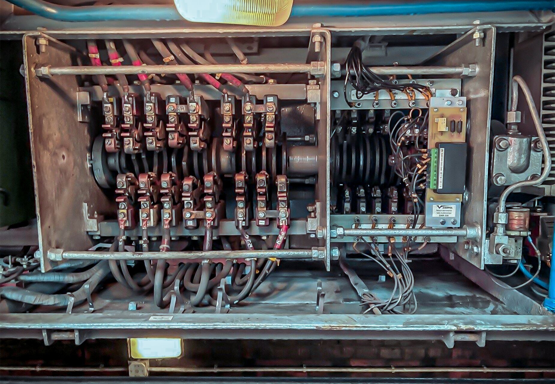 Zdjęcie przedstawia wał kułakowy. Widoczne są trzy płyty wsporne ramy, dwie po bokach i jedna w jednej trzeciej długości wału, licząc od lewej strony. Przed lewą płytą zamontowany jest cylinder pneumatyczny. Za tą samą płytą widać element elektroniczny umieszczony powyżej przekładni zębatej. Wał posiada dwadzieścia sześć styczników, dziesięć z lewej strony i szesnaście z prawej. Od wszystkich styczników odchodzą kable.