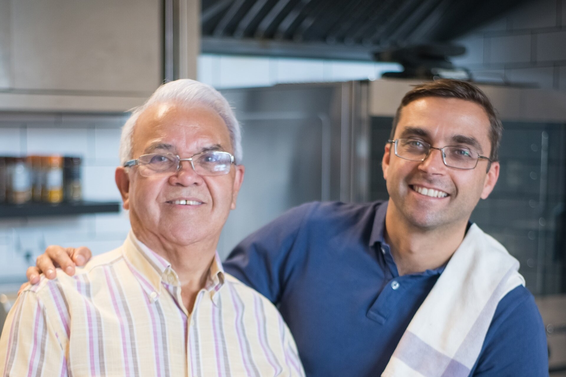 Zdjęcie przedstawia dorosłego mężczyznę i jego ojca. Obaj noszą okulary, mają podobne rysy twarzy. Mają inny kształt nosów. Ojciec jest już siwy, syn ma ciemne włosy. 