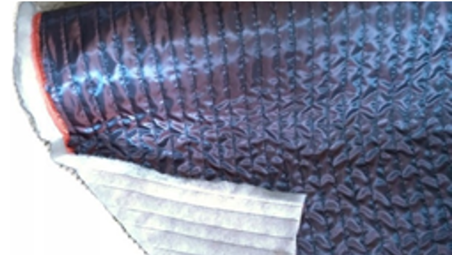 Na zdjęciu widoczny jest fragment materiału w kolorze metalicznie niebiesko‑szarym, jest on pikowany. Lewa strona jest biała.Nagranie tożsame z treścią.