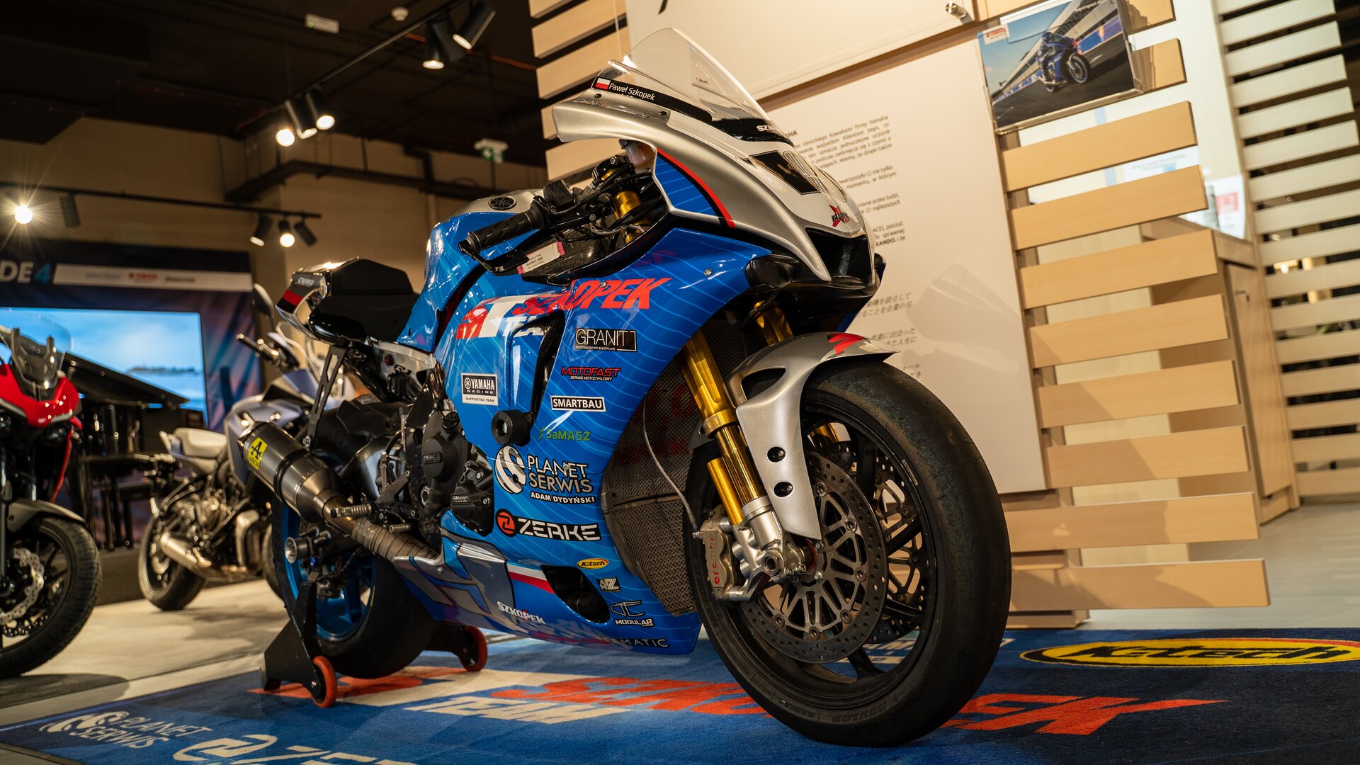 Zdjęcie przedstawia przód motocykla. Tam niebieskie osłony. Widoczna krótka szyba czołowa.  