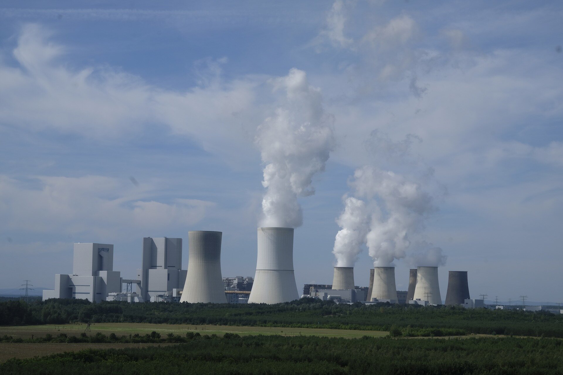 Zdjęcie poglądowe przedstawia przemysłowy pejzaż z ogromnymi kominami, z których wydobywa się biały dym.