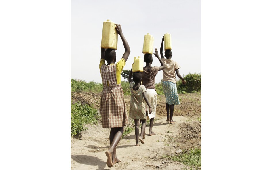 Zdjęcie przedstawia czarnoskóre dziewczynki, które niosą na głowach kanistry pełne wody. Uganda, Afryka.