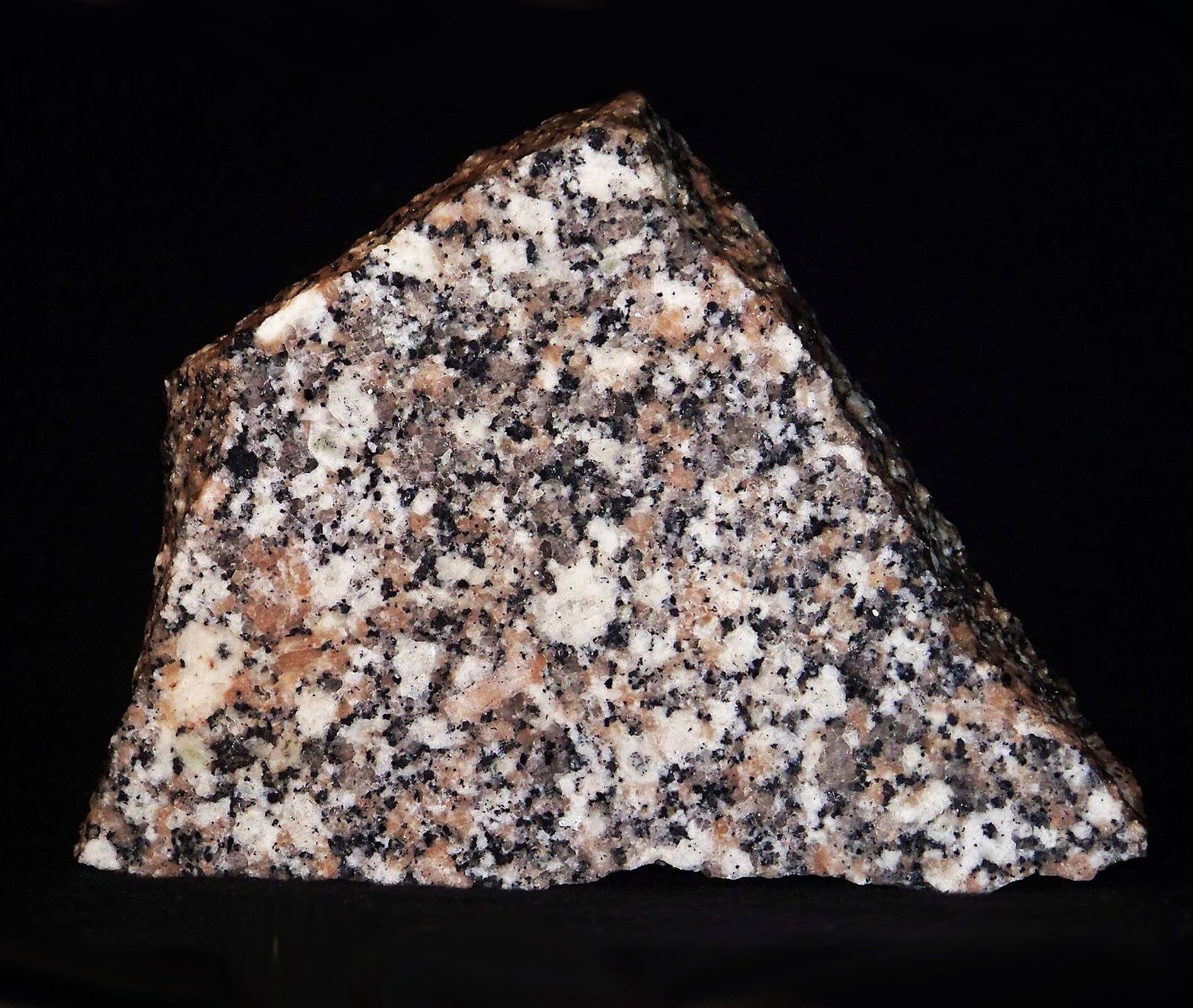 Fotografia prezentuje granit składający się z białych, czerwonych i czarnych minerałów, skała o budowie jawnokrystalicznej. Granit ma nierównomierny kształt naturalnej skały. Poszczególne minerały wchodzące w jego skład tworzą melanżową strukturę.