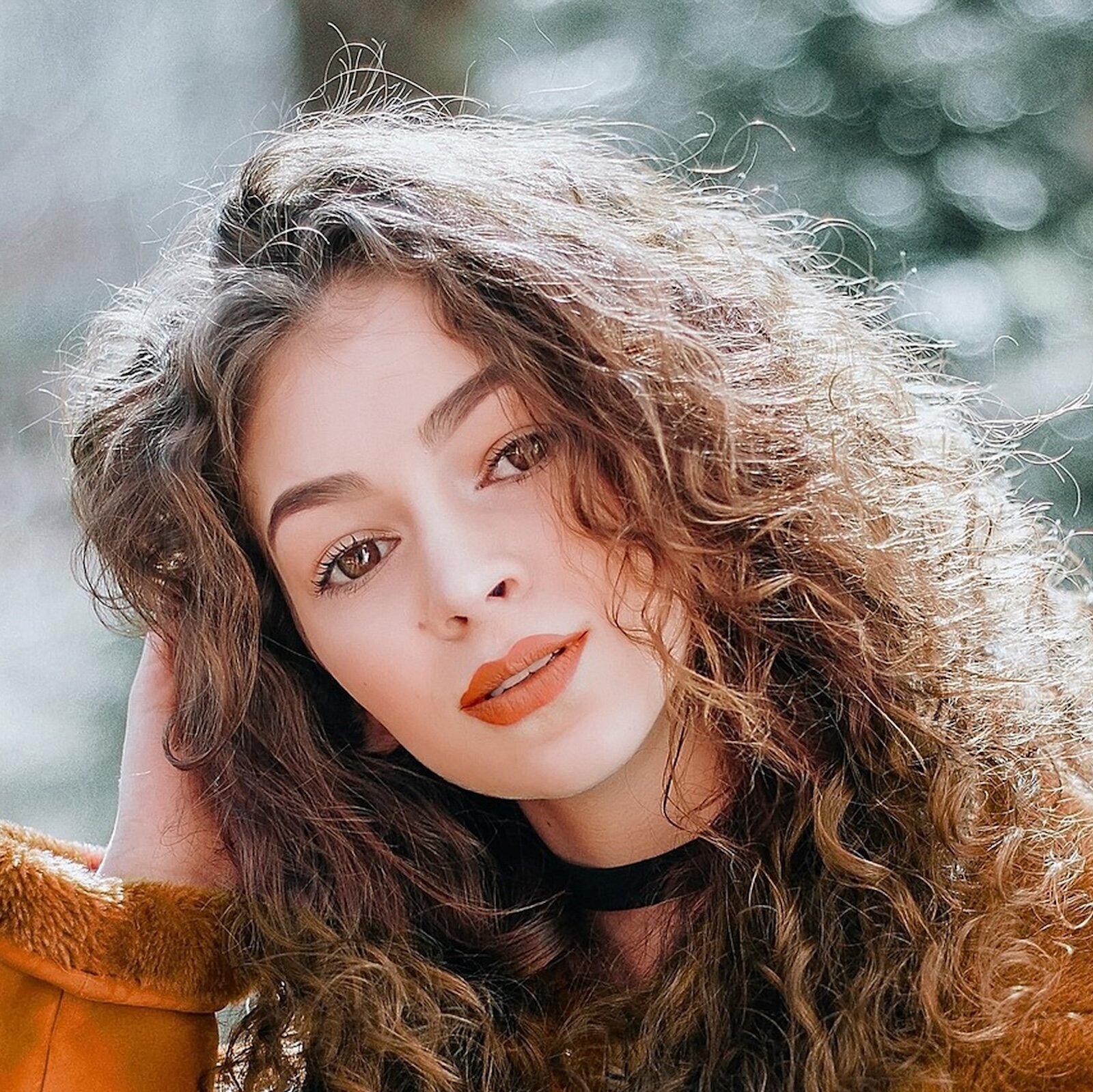 Grafika przedstawia portret dziewczyny o jasnej karnacji, ciemnych, długich, kręconych włosach i brązowych oczach. Głowę opiera na prawej ręce. Patrzy w obiektyw.