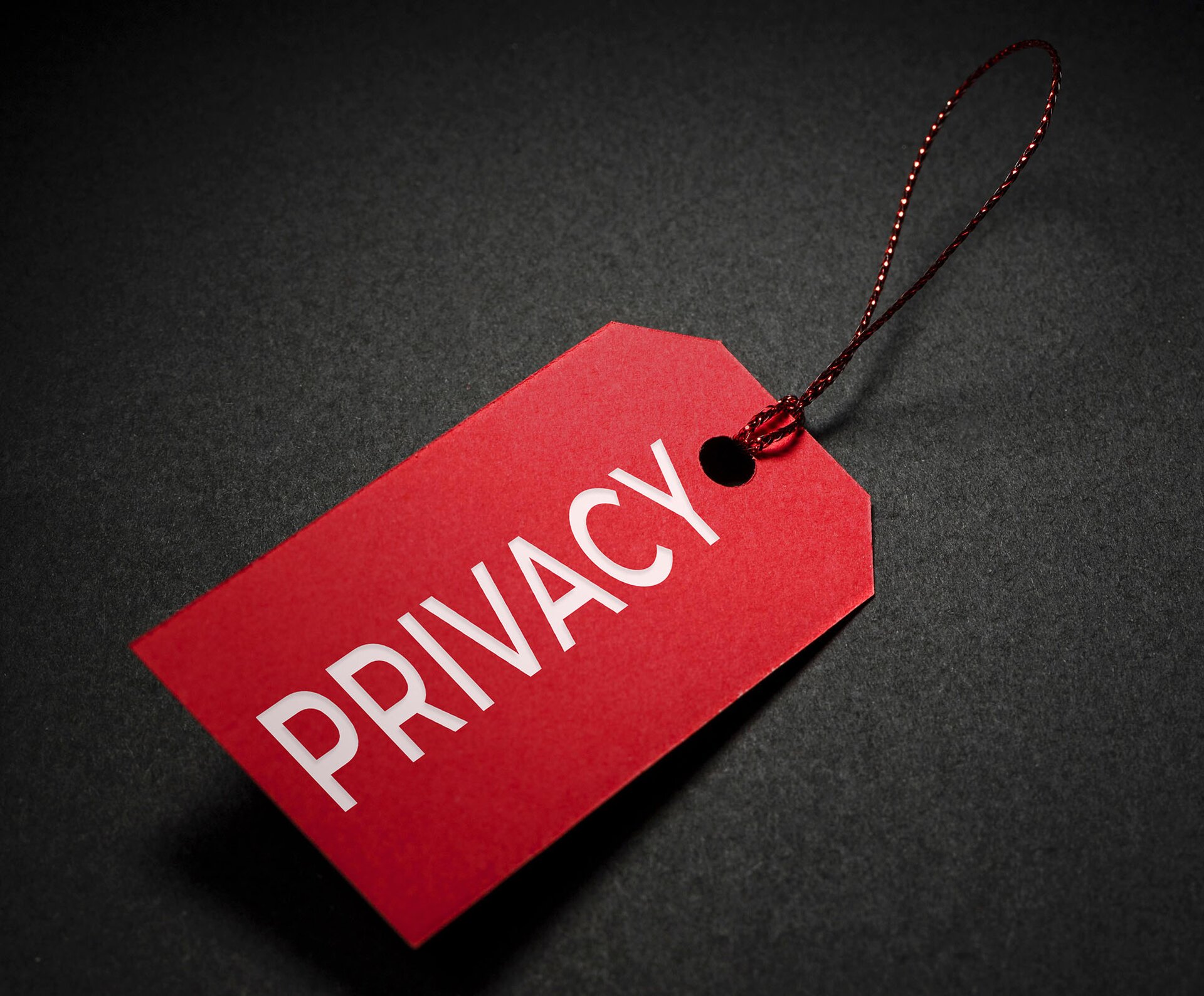 Zdjęcie przedstawia czerwoną zawieszkę z napisem "PRIVACY" położoną na czarnym tle.