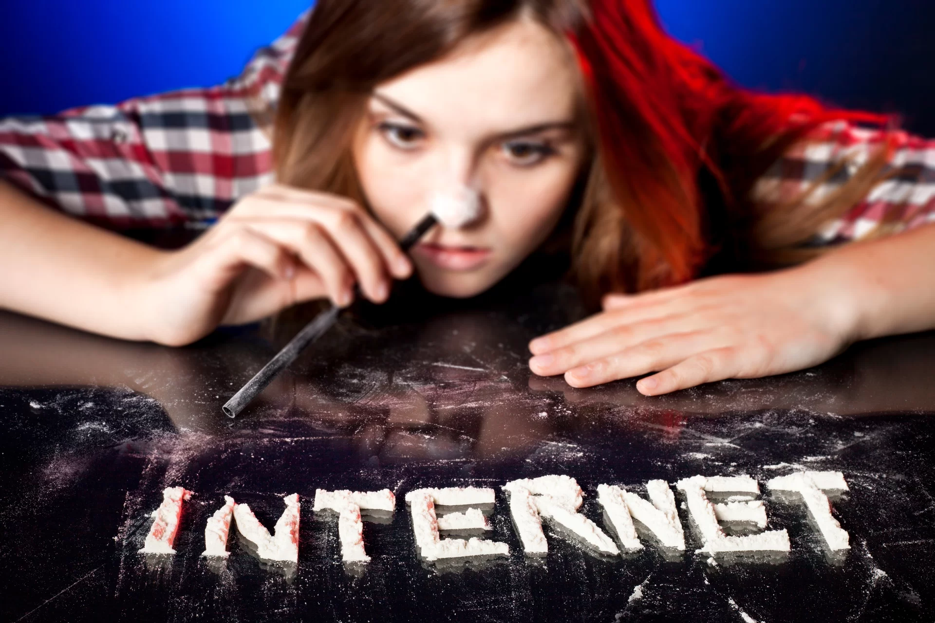 Ilustracja przedstawia uzależnienie do Internetu. Zdjęcie ukazuje młodą dziewczynę w czerwonych włosach, która zażywa przez nos białą substancję usypaną na stole na kształt słowa INTERNET.