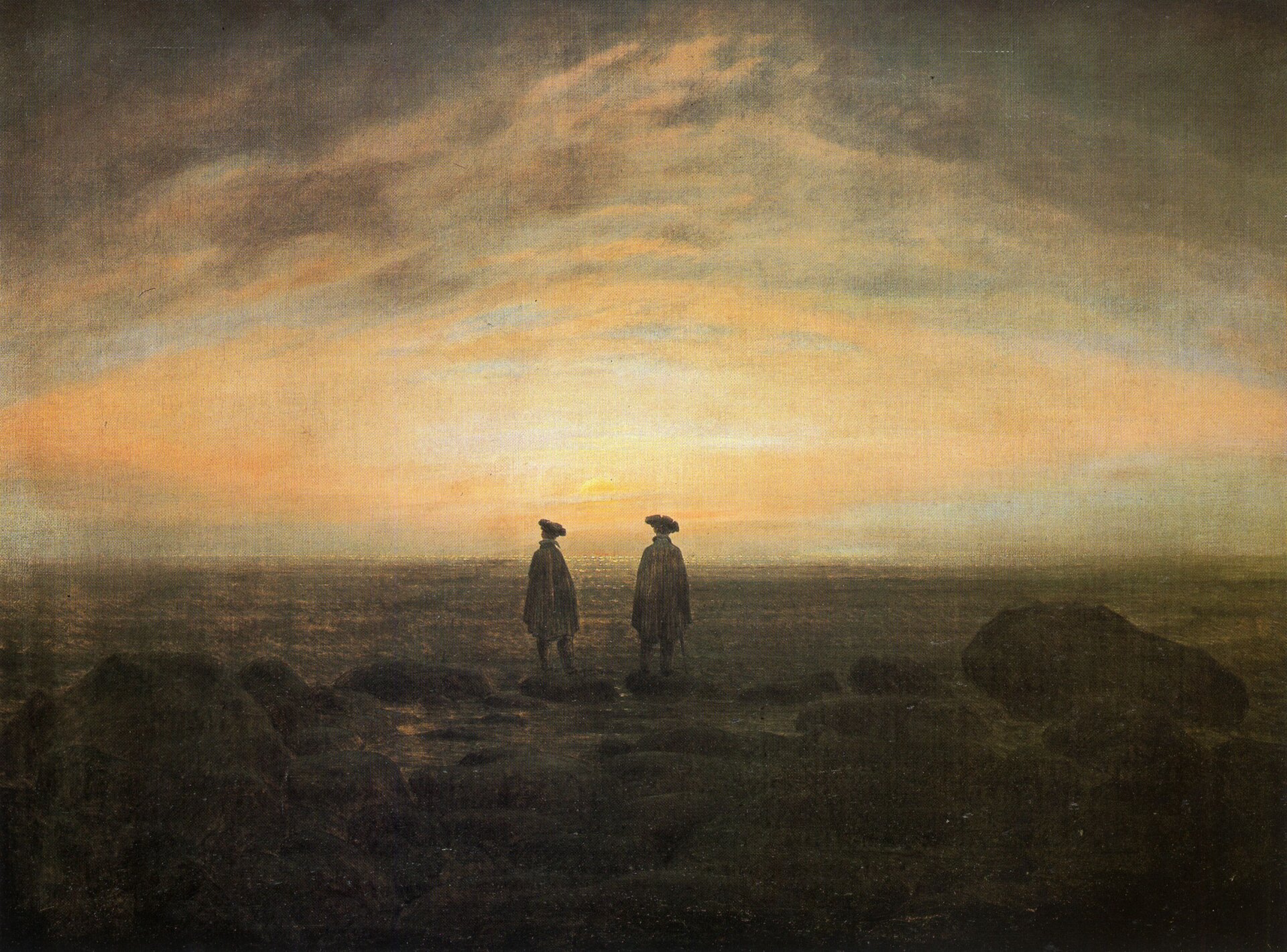 Ilustracja przedstawia obraz, na którym znajdują się dwaj mężczyźni. Mężczyźni stoją obok siebie, na brzegu morza. Dookoła nich jest pusto. Ubrani są oni w peleryny, na głowie mają kapelusze. Na drugim planie, na niebie wschód słońca. Im bliżej miejsca, w którym słońce wschodzi, tym niebo jest jaśniejsze.