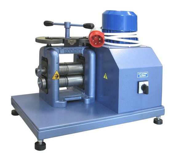 Ilustracja przedstawia walcarke stołową, podstawa walcarki składa się z prostokąta z czterema krótkimi nogami. Jest to metalowe urządzenie Na podstawie znajduje się skrzynka w kształcie graniastosłupa o podstawie romb. Na widocznej ścianie bocznej posiada włącznik. W górnej podstawie rombu znajduję się figura. Jest to walec, wokół niego zawinięty jest kabel siłowy.  Od skrzynki wychodzą dwa walce służące do nadawania kształtu danemu materiałowi. Nad nimi widnieje pokrętło.