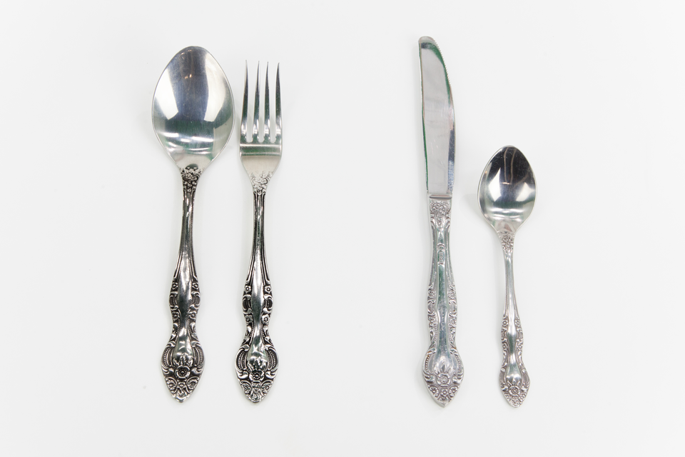 Na zdjęciu po lewej stronie widoczne są srebrna łyżka i srebrny widelec pokryte są szaroczarnym nalotem, po prawej stronie zdjęcia znajdują się srebrny nóż oraz srebrna łyżeczka po oczyszczeniu, nie widać na nich ciemnego nalotu, błyszczą się. 