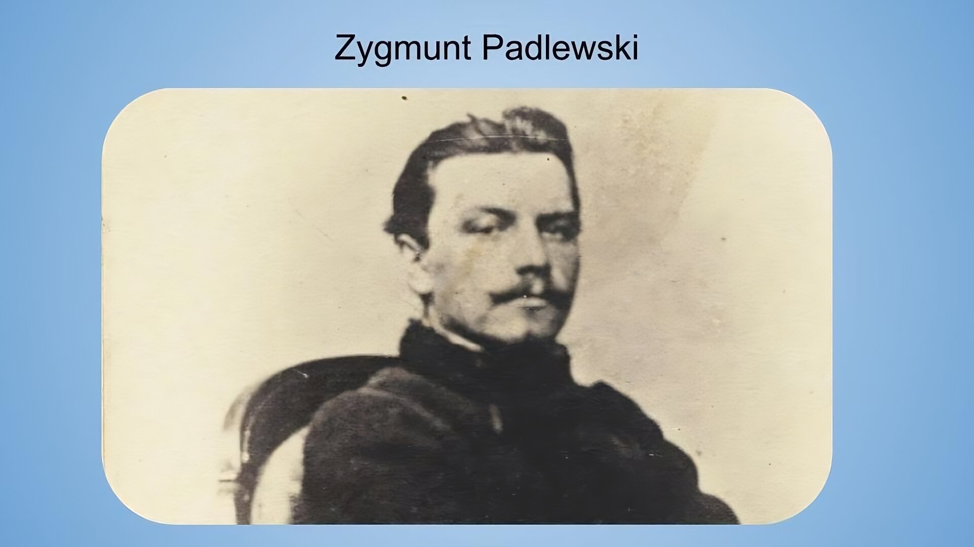 Jasnoniebieskie tło. Na górze napis: Zygmunt Padlewski. Poniżej czarno‑biała fotografia przedstawiająca mężczyznę w średnim wieku o ciemnych, zaczesanych do tyłu wlosach i ciemnych wąsach. Mężczyzna ubrany jest w ciemny płaszcz z kołnierzem, a jego plecy spoczywają na półokrągłym oparciu krzesła. Mężczyzna patrzy wprost do kamery.