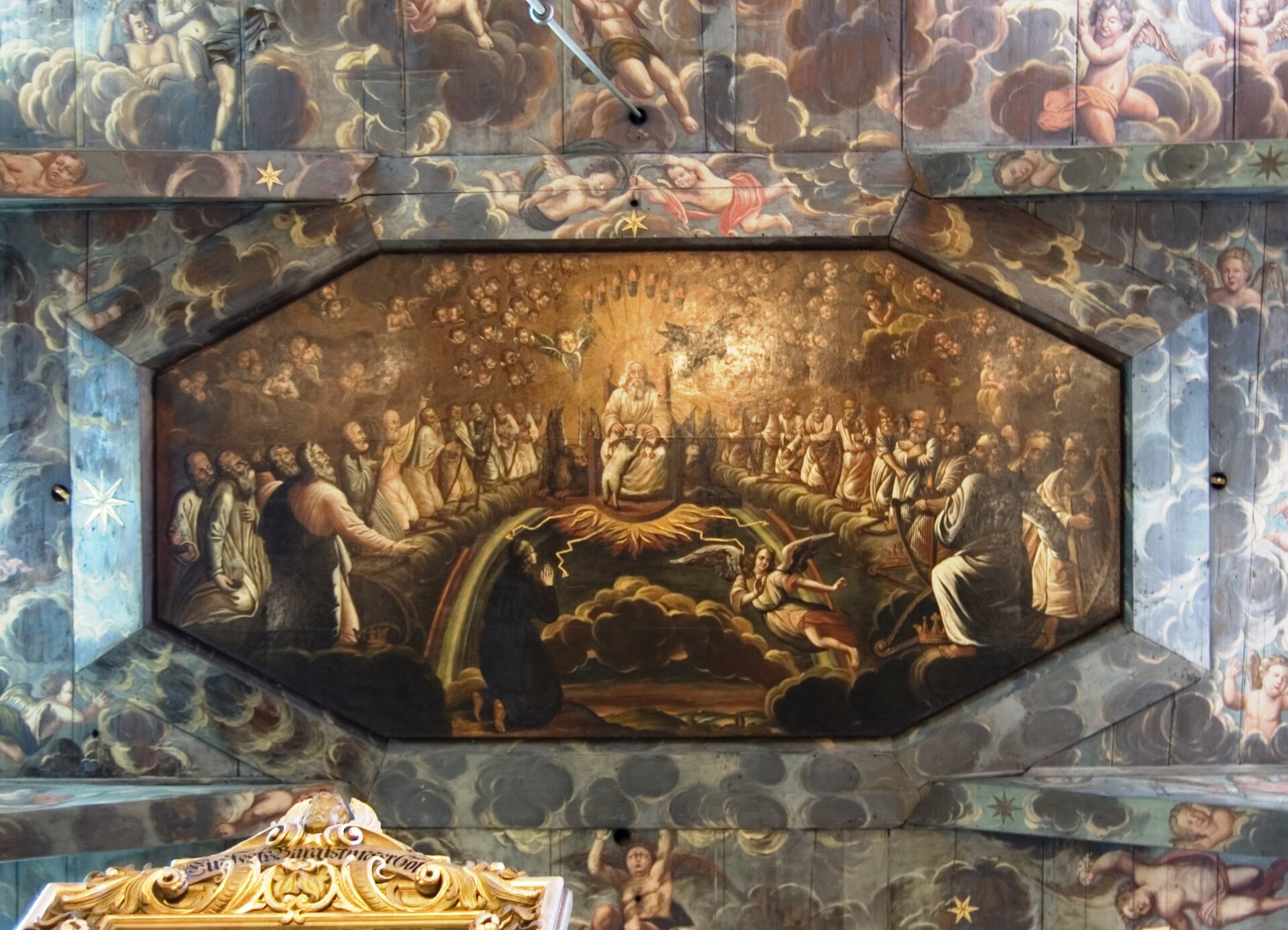 Ilustracja przedstawia malowidło pokrywające drewniany sufit. Pośrodku sufitu znajduje się podłużne, ośmiokątne wgłębienie. Otoczone jest wyobrażeniem licznych chmur i unoszącymi się między nimi aniołów. Malowidło umieszczone na ośmiokącie ukazuje brodatego starca siedzącego na tronie. Wokół głowy mężczyzny roztacza się blask. Jest to Bóg Ojciec. Unosi się nad Nim para aniołów. O Jego kolana opiera się pies stojący na tylnych nogach. Wokół tronu klęczą mężczyźni. Unoszą się na chmurach. Są ubrani w luźne, jasne szaty. Pod tronem rozciąga się fragment nieba. Ukazane są błyskawice, tęcza i ciemne chmury. Na jednej z nich klęczy bosy mężczyzna ubrany w czarną szatę. Składa ręce do modlitwy. Unosi głowę.