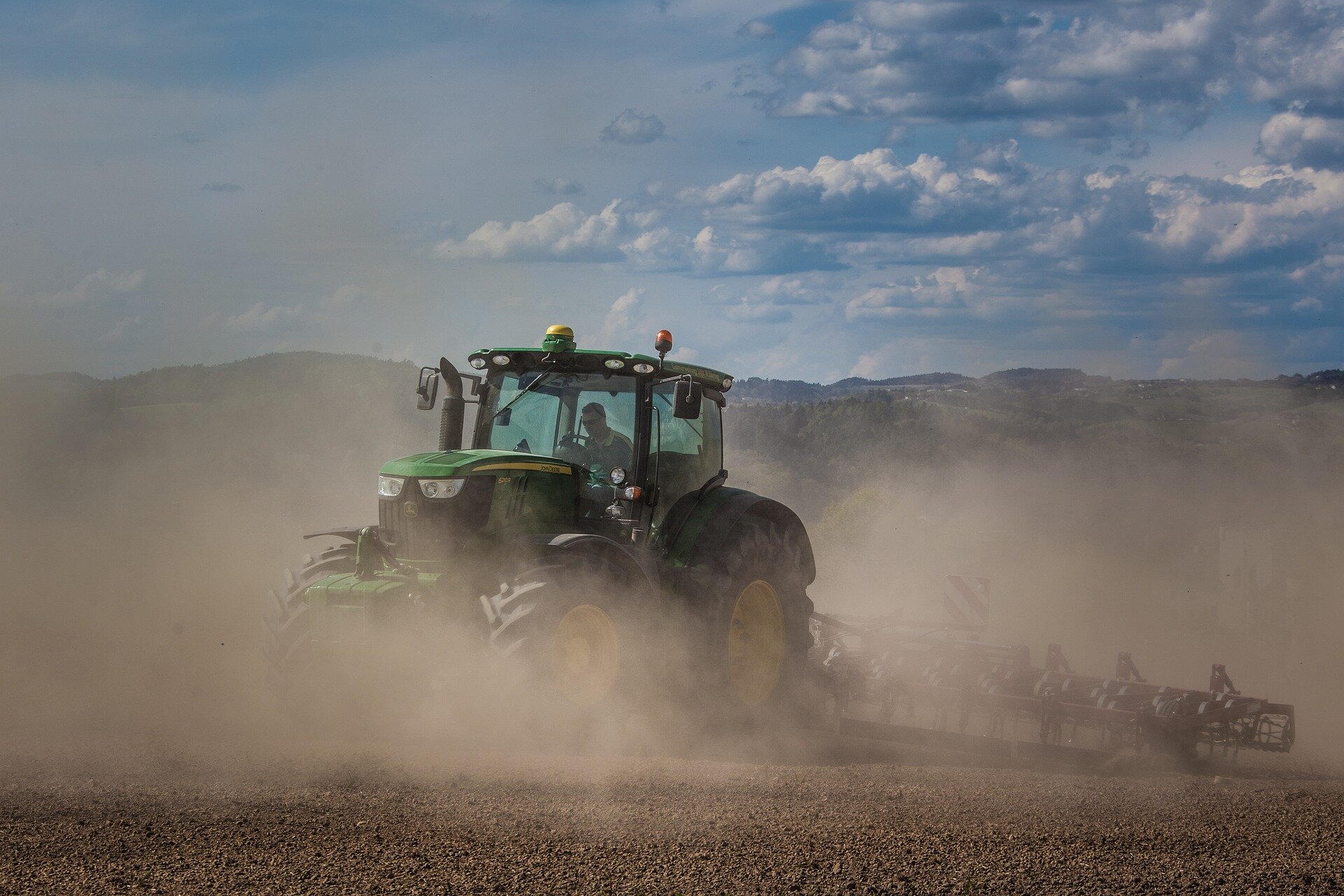 Zdjęcie przedstawiające traktor uprawiający pole w trakcie suszy, przez co dookoła unosi się bardzo duża ilość gęstego pyłu ograniczającego widoczność.
