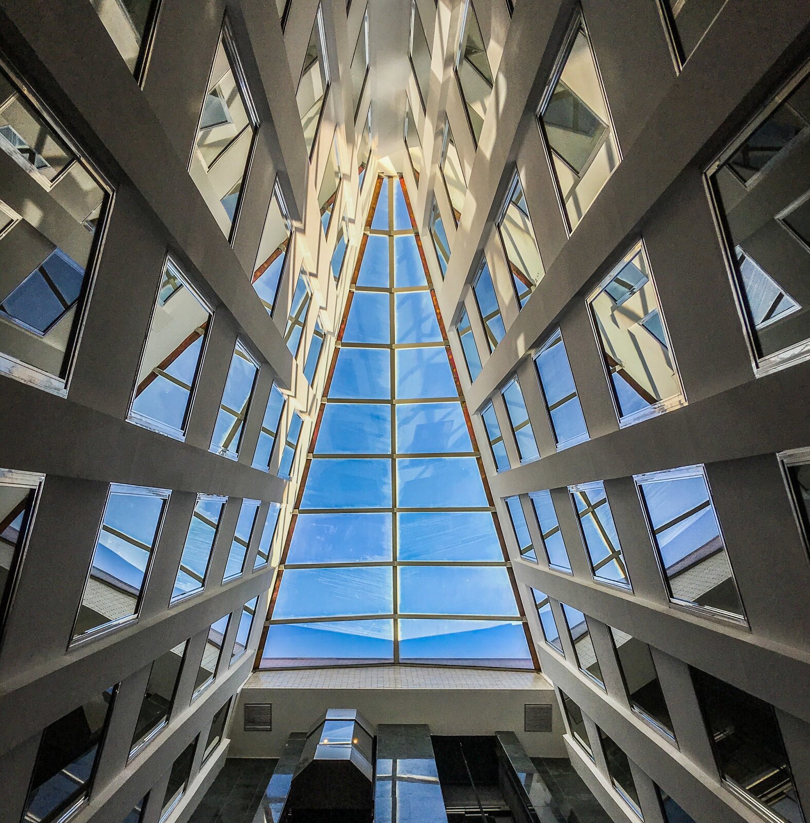 Ilustracja przedstawia oszklony dach budynku w kształcie trójkąta równoramiennego. 