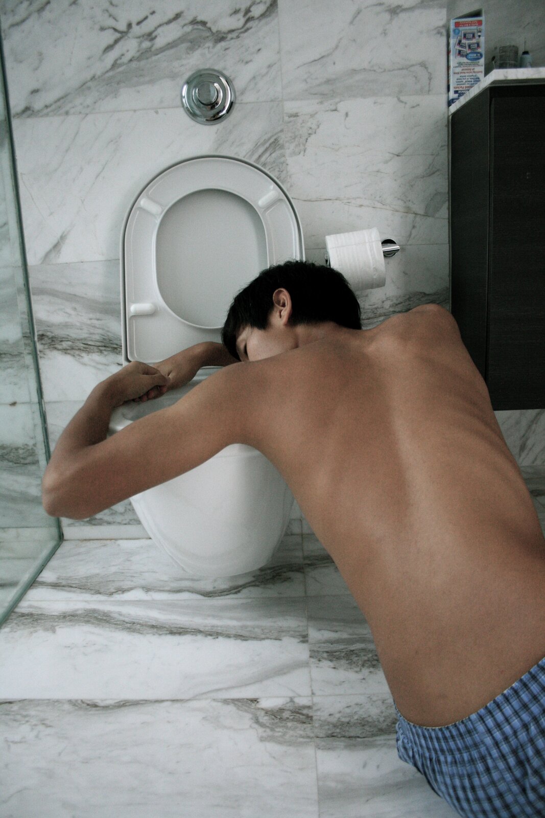 Zdjęcie przedstawia młodego chłopaka pochylającego się nad toaletą w celu wymiotowania.