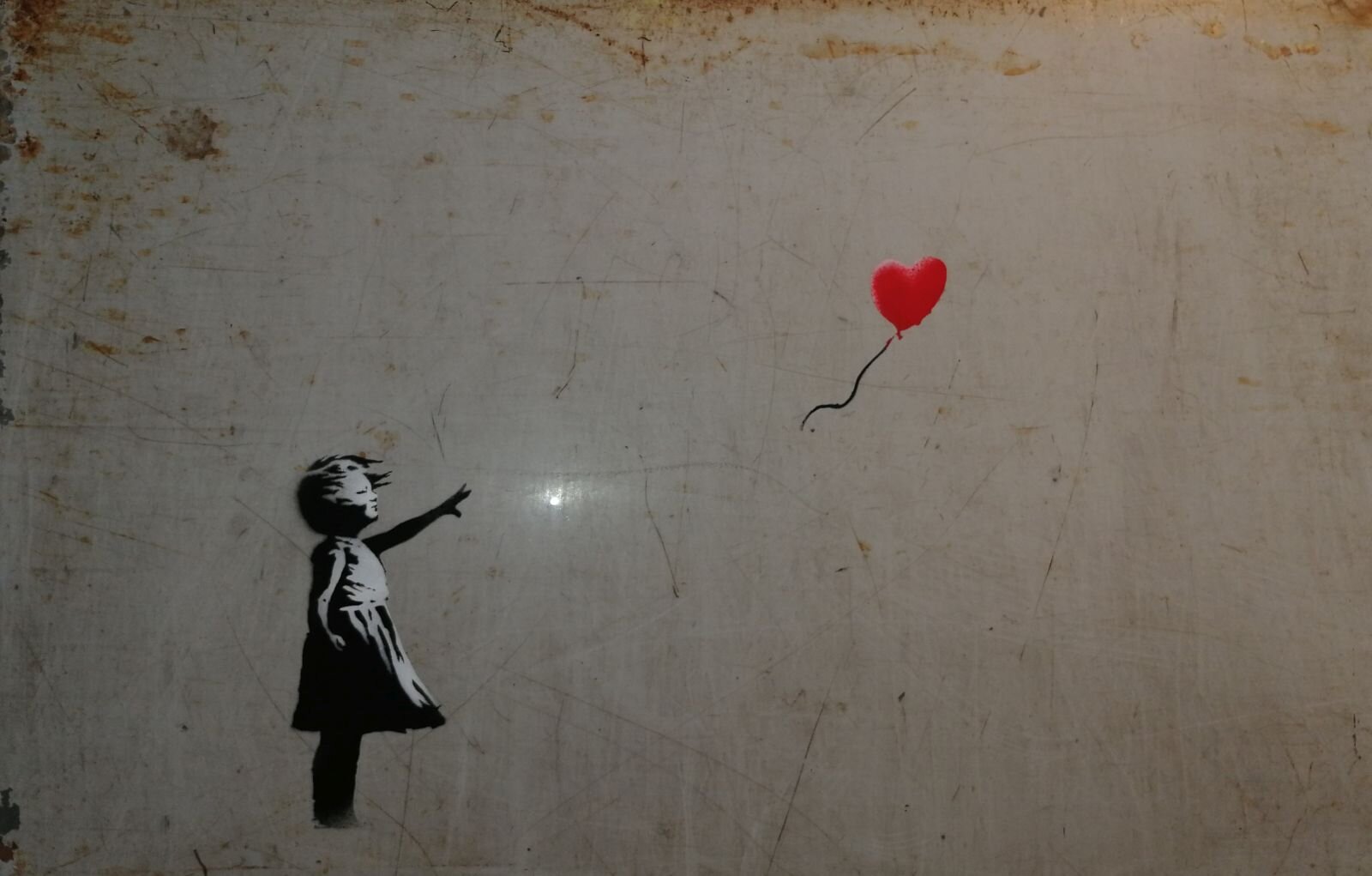 Zdjęcie przedstawia dzieło street art [czytaj: strit art] Banksy'ego [czytaj: banksiego], wykonane za pomocą szablonu na murze. Z lewej strony znajduje się mała dziewczynka, której kontury namalowano czarnym kolorem. Jest ubrana w sukienkę do kolan, lewą rękę wyciągnęła w kierunku uciekającego na prawą stronę czerwonego balonika na sznurku w kształcie serca. 