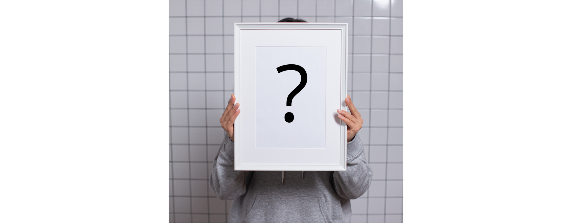 Zdjęcie przedstawia osobę, która trzyma przed sobą dużą ramkę na zdjęcie. Ramką zasłania swoją twarz. W ramce zamiast zdjęcia znajduje się duży znak zapytania.