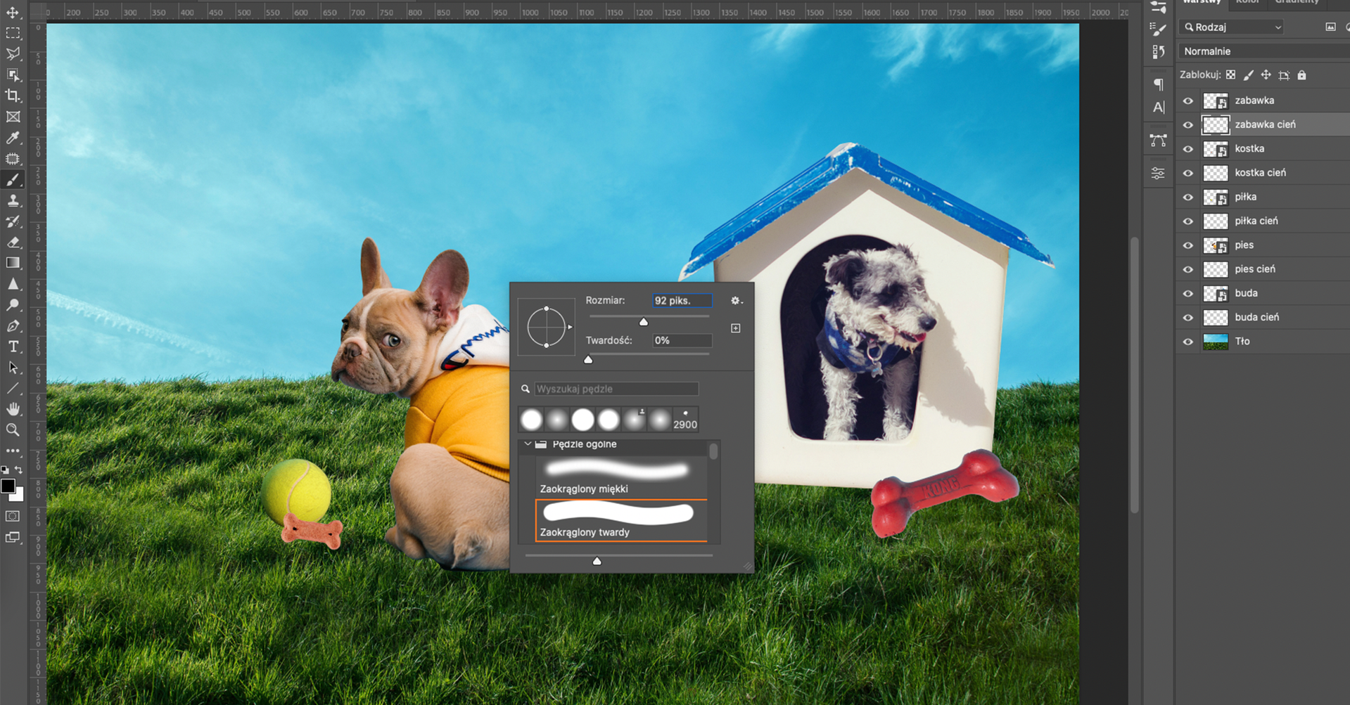 Ilustracja przedstawia okno programu. W obszarze roboczym jest prostokąt. Wypełnia go zdjęcie trawy z błękitnym niebem. Po prawej stronie zdjęcia jest buda, z której łeb wystawia mały pies. Buda jest biała, ma niebieski dach. Po jej prawej stronie na dole znajduje się mała kość - zabawka. Po lewej stronie budy siedzi buldog francuski. Ma na sobie psie ubranko. Jego łeb jest po lewej stronie, patrzy na obserwatora. Poniżej psa na trawie leży piłka tenisowa, a przy niej kość - smaczek. Na tle fotomontażu jest okno dotyczące wyboru pędzla. Wybrano pędzle zaokrąglony twardy.  Po prawej stronie jest panel dotyczący Warstw. Warstwami są kolejno: zabawka, zabawka cień, piłka, piłka cień,  pies, pies cień, kostka, kostka cień,  buda, buda cień,  tło. Zaznaczono zabawka cień. 
