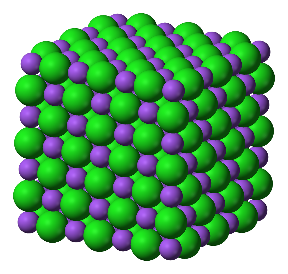 Ilustracja przedstawia kryształ jonowy chlorku sodu, w którym kationy sodu (fioletowe kulki) i aniony chloru (zielone kulki) są ułożone naprzemiennie i tworzą sześcian.