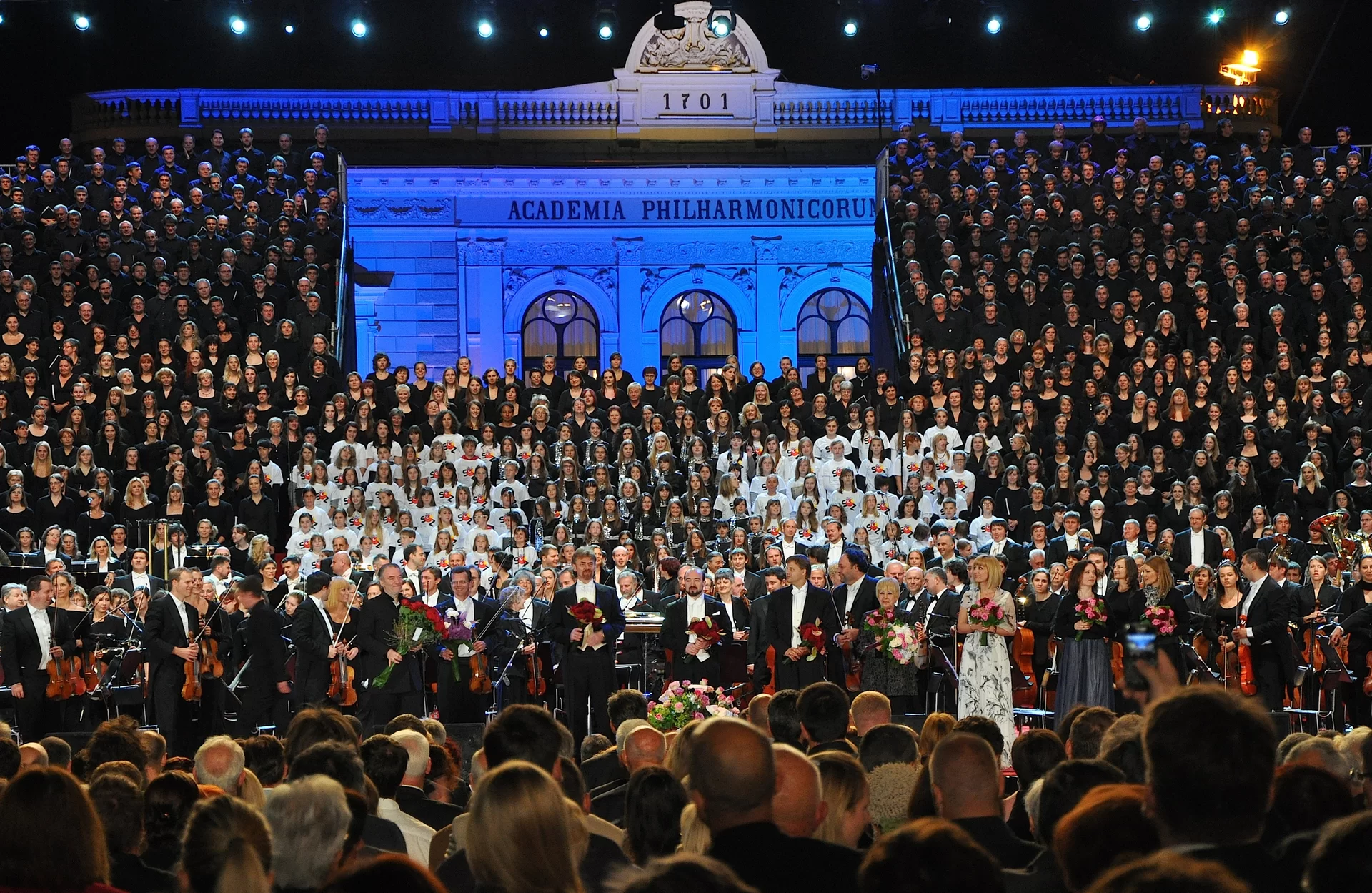 Ilustracja przedstawia: 1083 muzyków w czasie wykonywania VIII Symfonii (Tysiąca) Gustava Mahlera w Ljubljanie, Słowenia. muzycy ubrani sa na czarno i biało. Z przodu fotografii widać ludzi z widowni, zwróconych w stronę orkiestry.