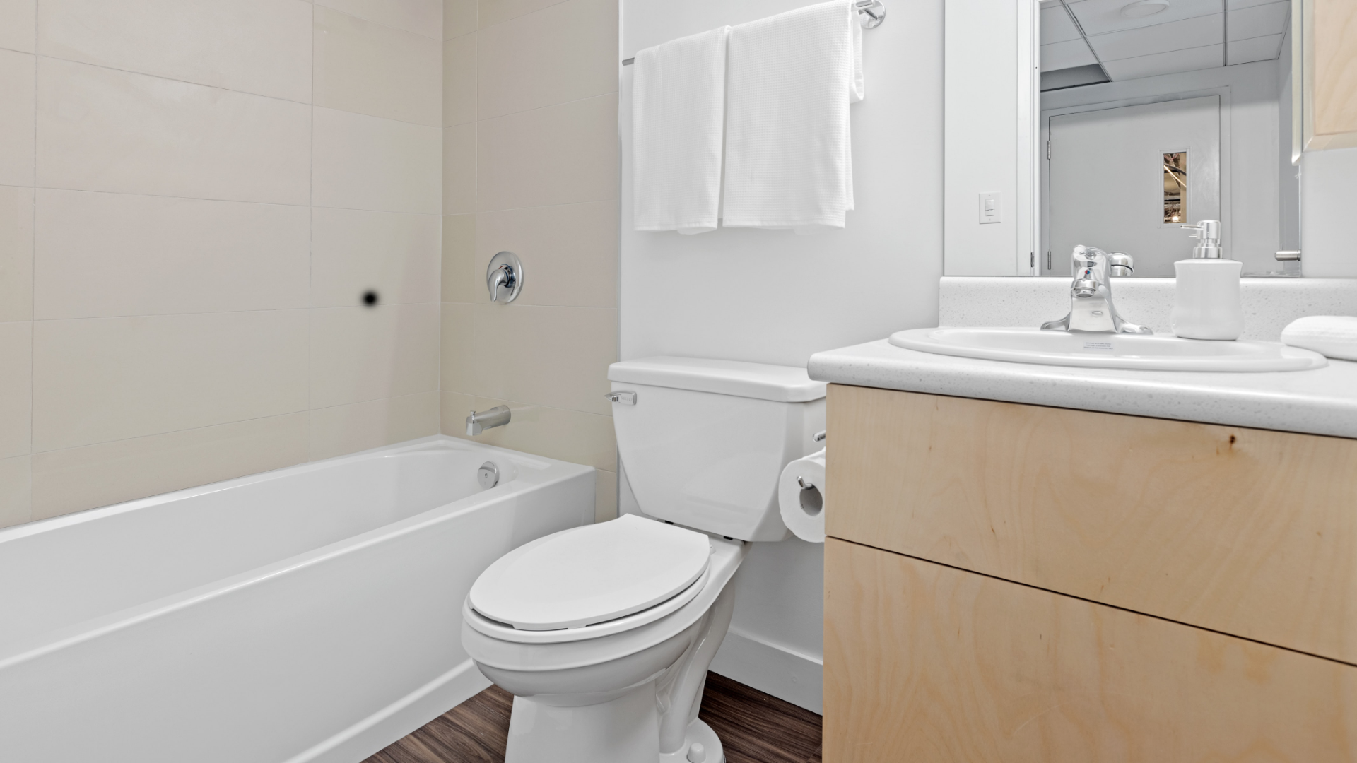 Zdjęcie przedstawia łazienkę. Po lewej stronie, przy ścianie znajduje się wanna. Obok wanny, po prawej stronie znajduje się muszla klozetowa. Po prawej stronie, obok muszli znajduje się szafka z umywalką.