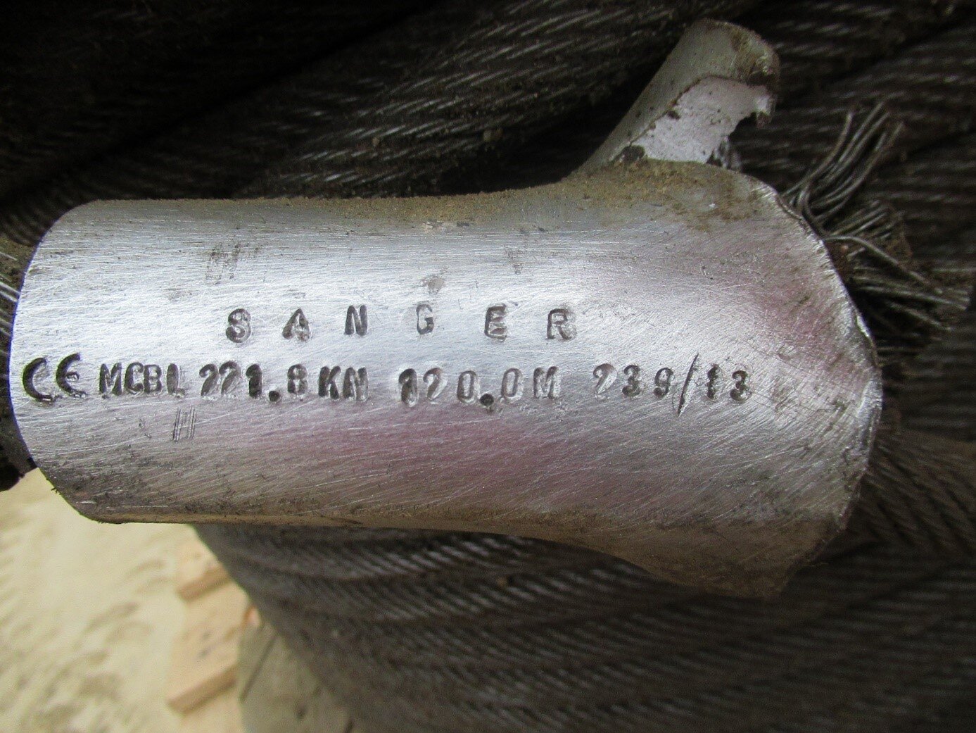Na zdjęciu przedstawiony jest fragment zawiesia z rozerwanym zakuciem uchwytu. Widoczny uchwyt zawiesia jest o kształcie cylindra. Cylinder po prawej stronie u góry jest rozerwany. Wystające splotki liny zawiesia mają przerwaną ciągłość. Na zakuciu uchwytu znajduje się wyżłobione oznaczenie: Sanger, oraz wyżłobiony numer seryjny. Początek numeru seryjnego: MCBL. Dalsze oznaczenia numeru są częściowo zdeformowane przez co nie są przytaczane. 