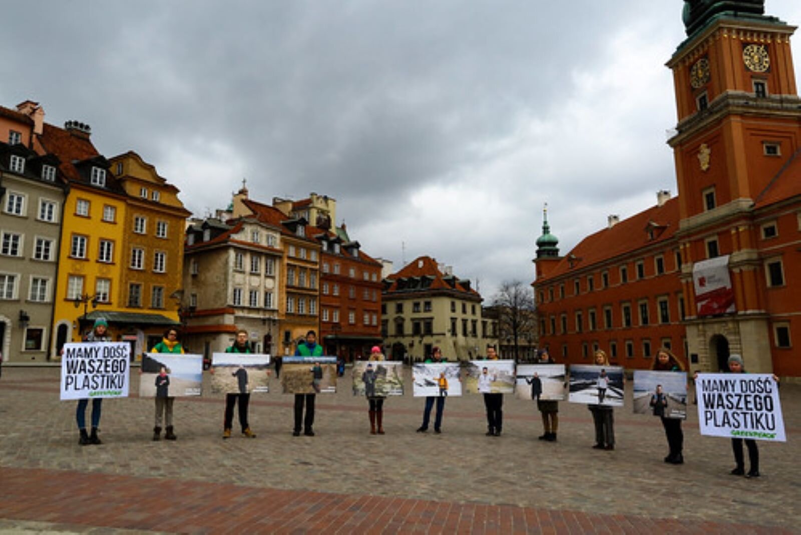 Na Placu Zamkowym w Warszawie odbywa się happening ekologiczny. 11 młodych działaczy Greenpeace (czyt.grinpis) stoi w półokręgu, skrajne osoby trzymają plansze z napisem; "Mamy dość waszego Plastiku!", pozostali trzymają plansze ze zdjęciami. Za nimi bryła Zamku Królewskiego w Warszawie i kamienice starego miasta.