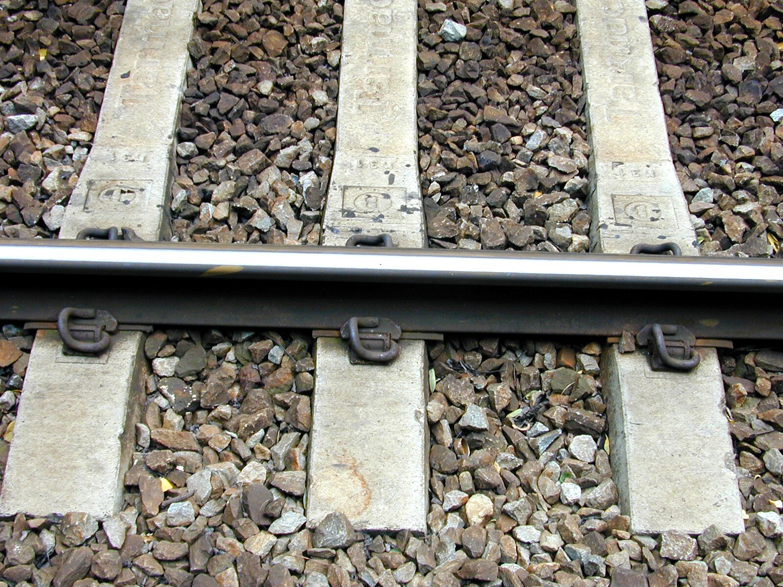 Zdjęcie przedstawia tory kolejowe. Pomiędzy drewnianymi podkładami kolejowymi wysypane są brązowe kamienie.