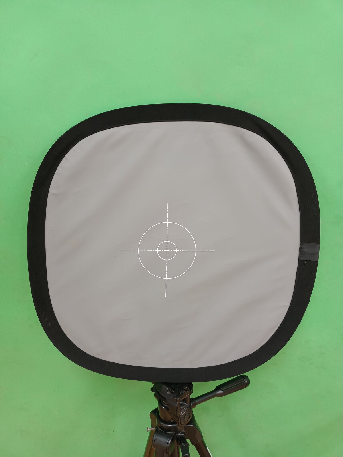 Zdjęcie przedstawia szarą kartę kalibracyjną, zamontowaną na statywie, karta ma zaznaczony swój środek.