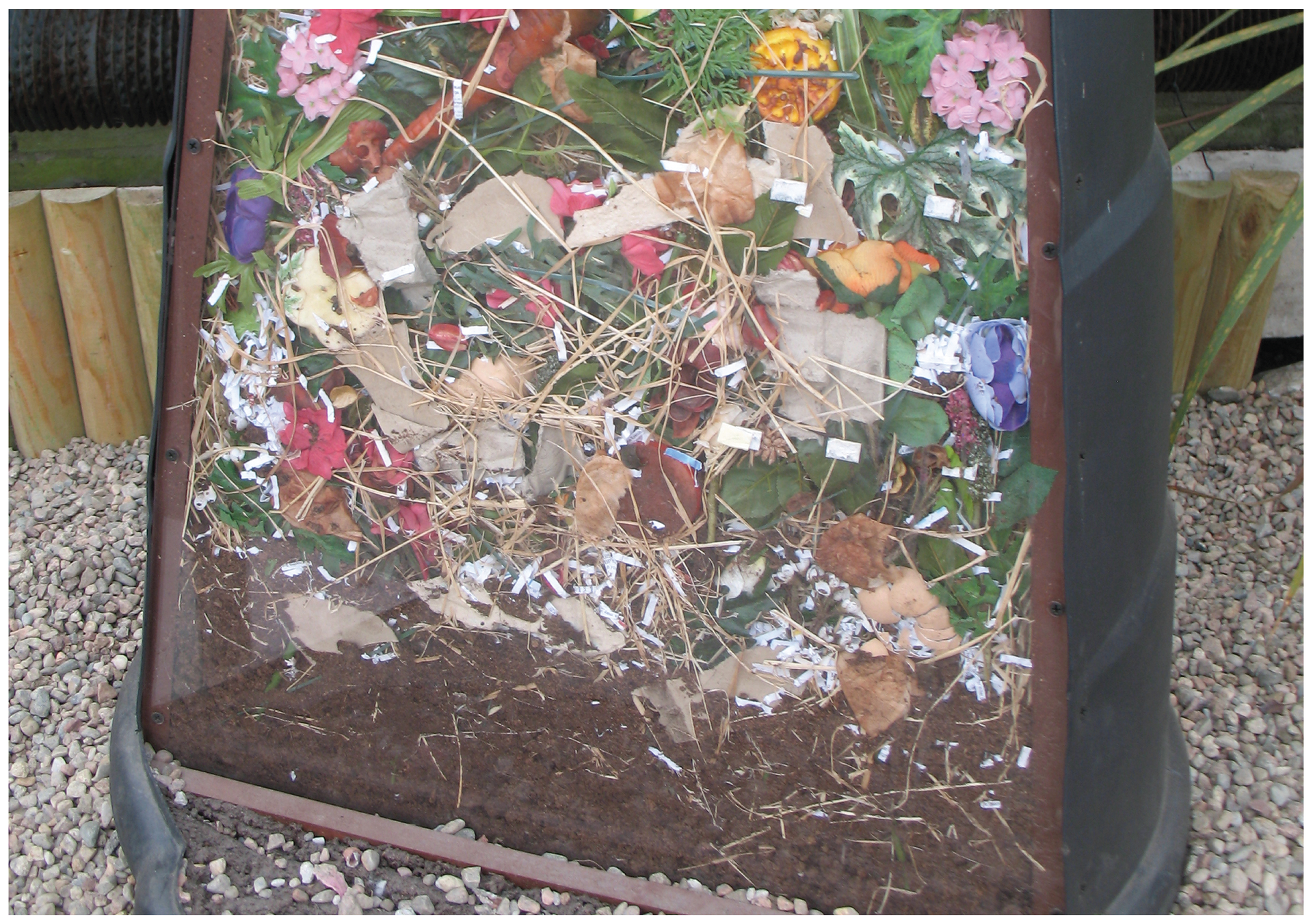 Fotografia przedstawia pojemnik z resztkami roślinnymi. Są tu kwiaty, liście, sucha trawa. Taki pojemnik to kompostownik. W nim bakterie rozkładają resztki, wytwarzając naturalny nawóz, czyli kompost. Można go wykorzystać na działce i na polu.