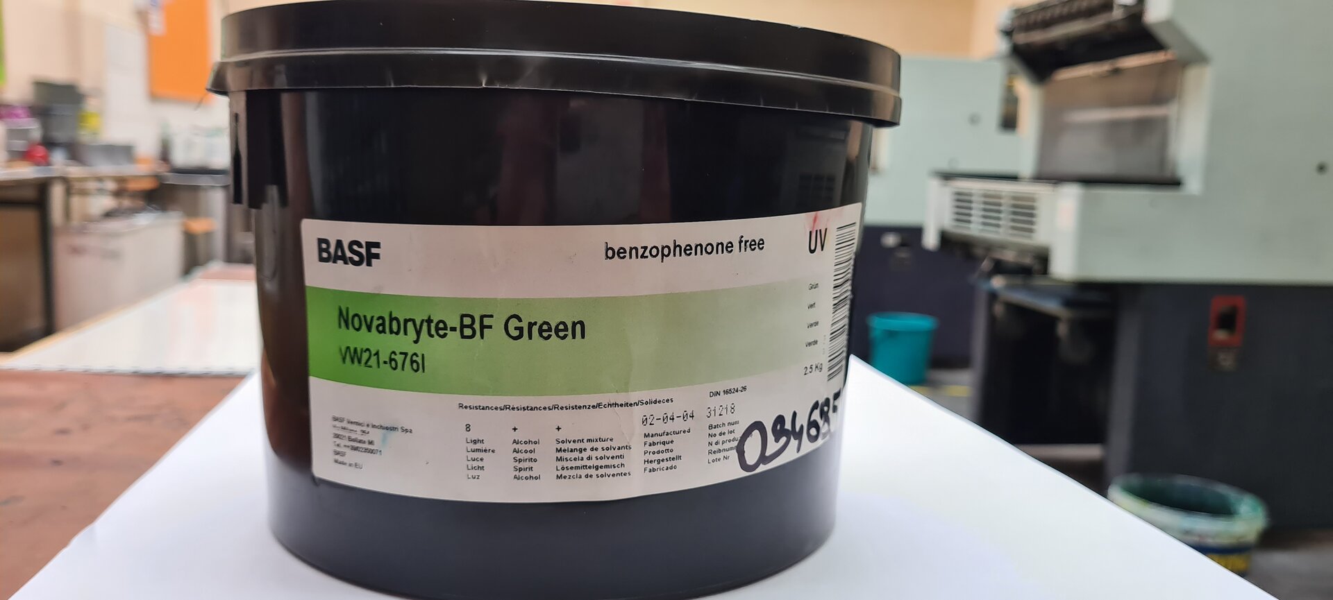 Zdjęcie przedstawia farby drukowe offsetowe. Widoczny jest duży cylindryczny czarny plastikowy pojemnik z uchwytem, na którym widoczna jest biała etykieta informacyjna z napisami.