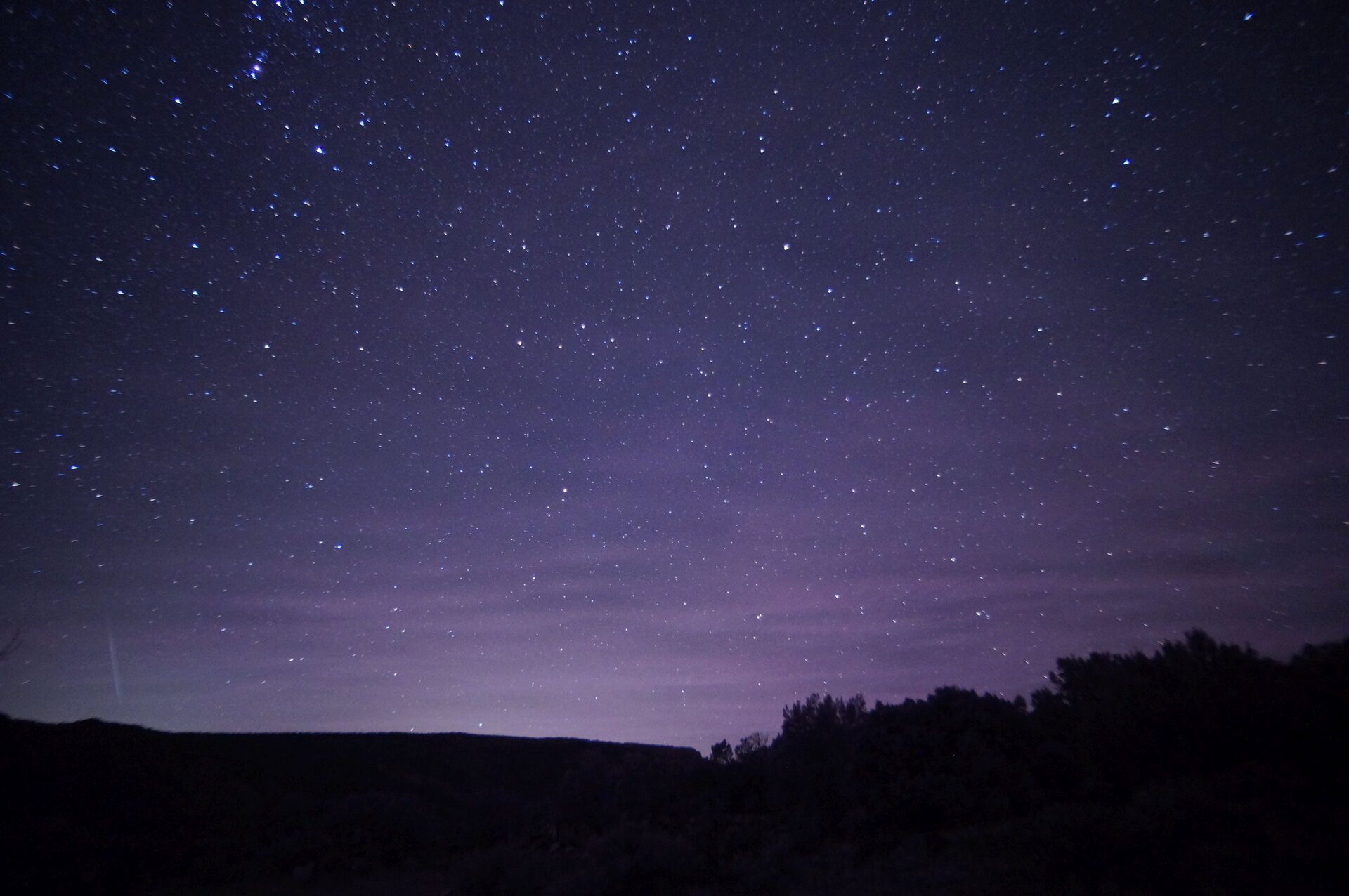 Ilustracja przedstawia gwieździste, fioletowo-granatowe niebo, które jest rozjaśnione w dolnej części. Poniżej znajduje się horyzontalny, czarny pejzaż.