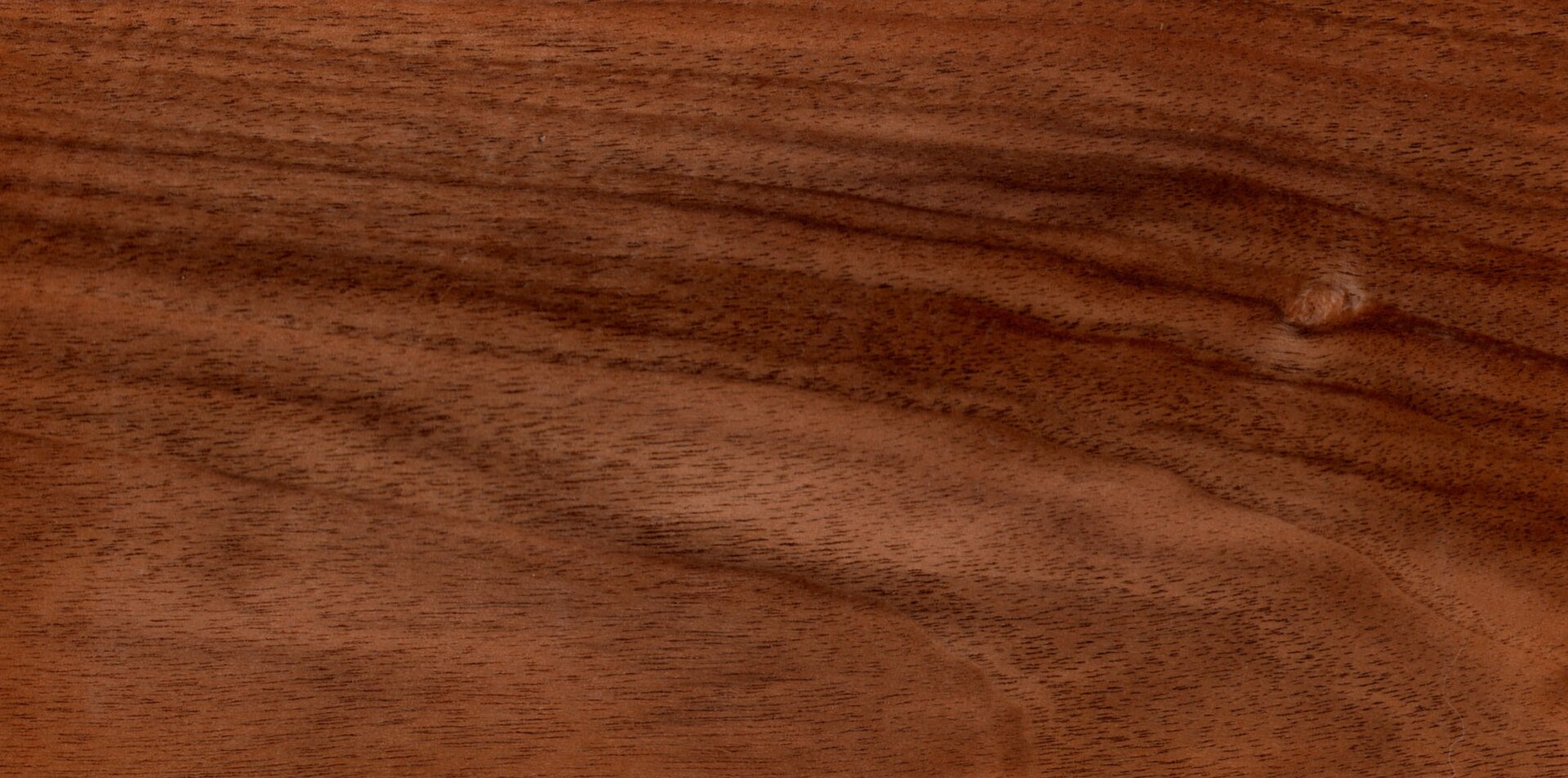 Zdjęcie przedstawia deskę z orzecha. Widoczna jest brunatno‑czerwona deska z ciemno brunatnymi słojami drewna.